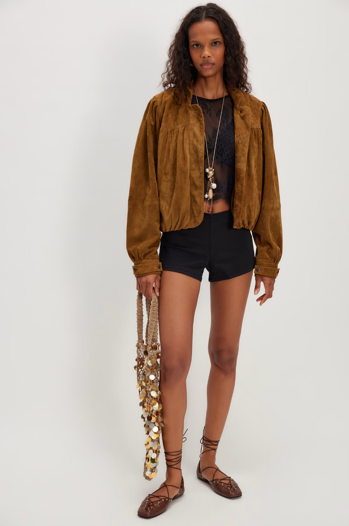 Woman wearing a Lunar Ash Lace Top in black sheer lace, paired with a brown jacket, shorts, and boho accessories.