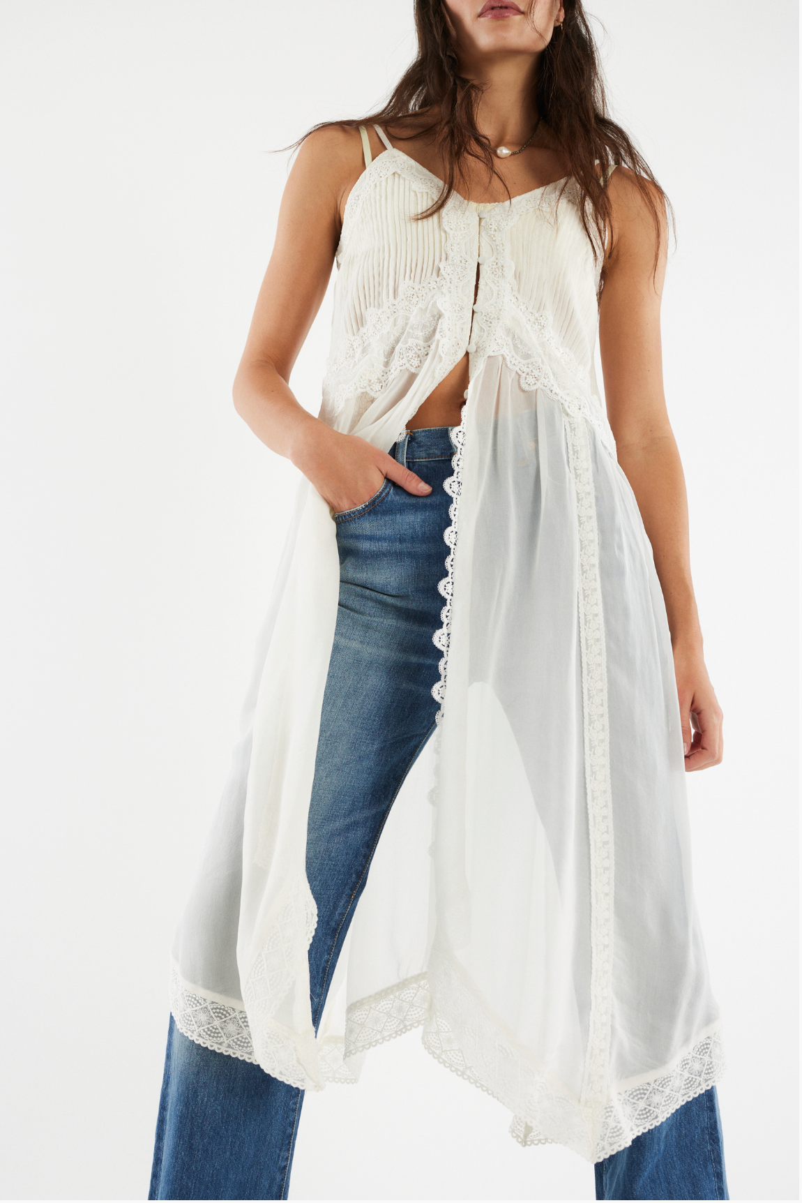 Woman wearing a flowing white Snowbird Maxi Top with lace details layered over blue jeans in a bright studio.