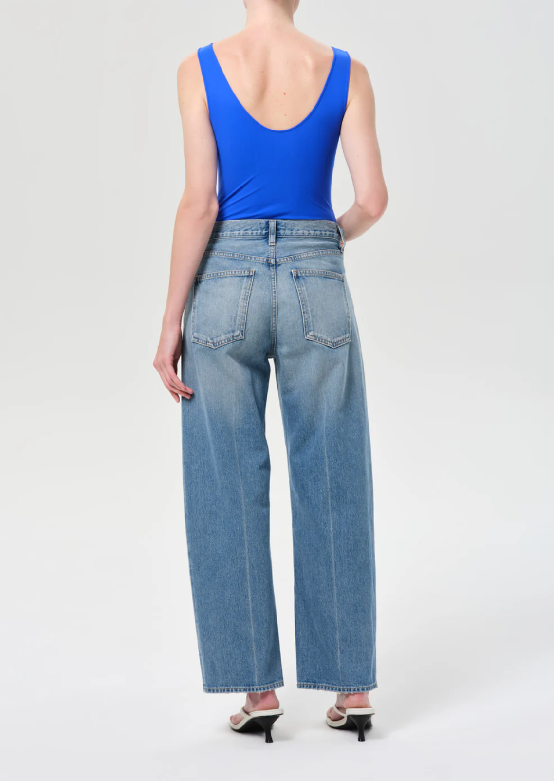 Back view of model wearing Arc Jean 29" In Brink by Agolde" loose straight leg denim jeans with a blue sleeveless top.