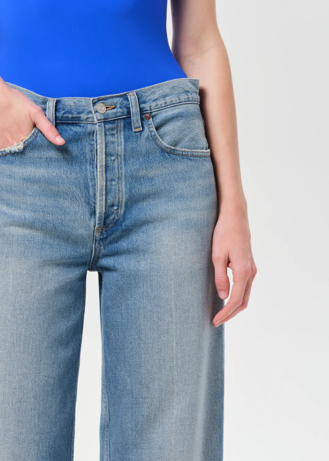 Close-up of a woman wearing "Arc Jean 29" In Brink by Agolde" light blue denim jeans with a blue top.