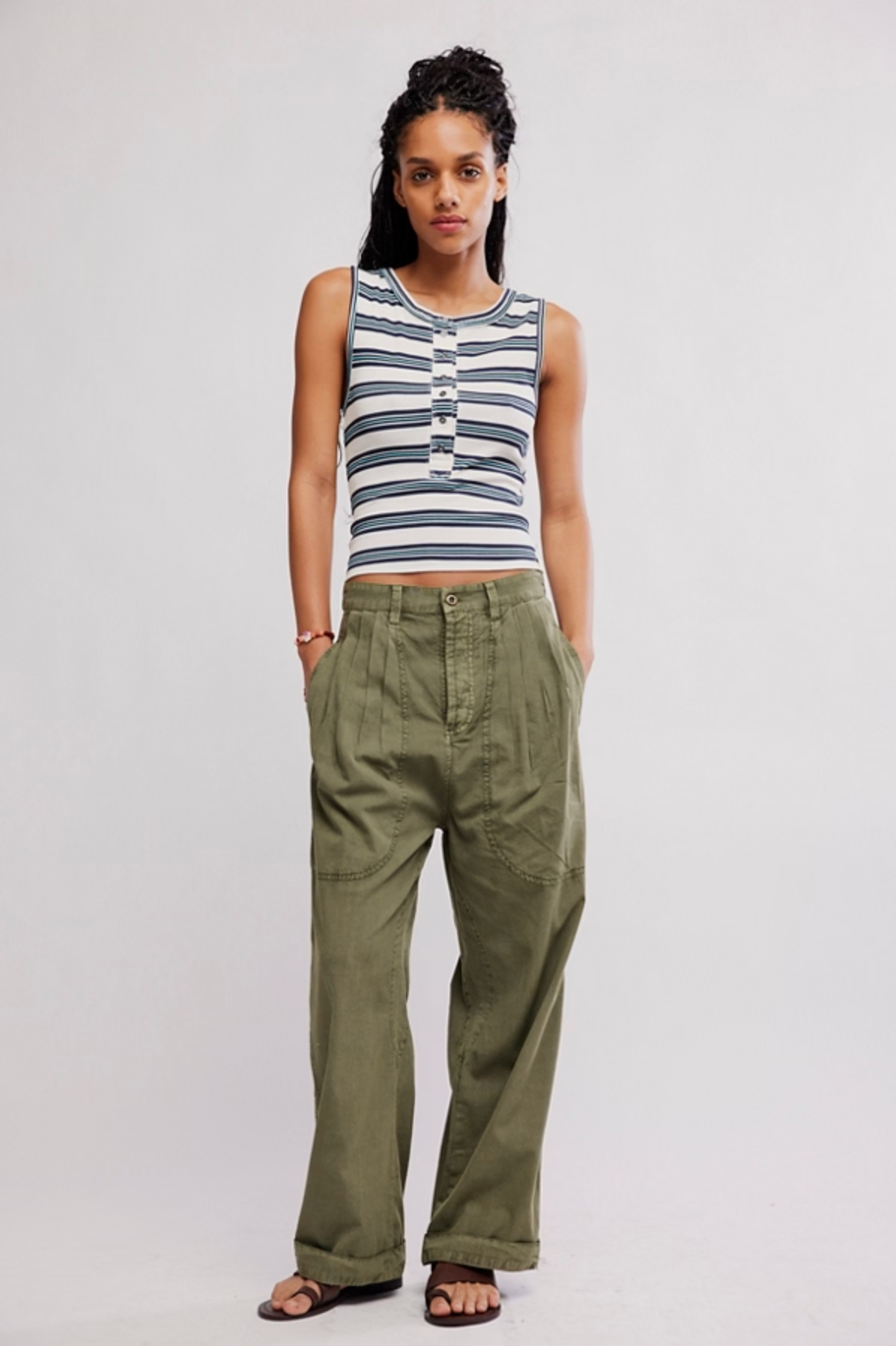Woman wearing olive green Clover Dropped Trouser by Free People with striped sleeveless top and sandals.