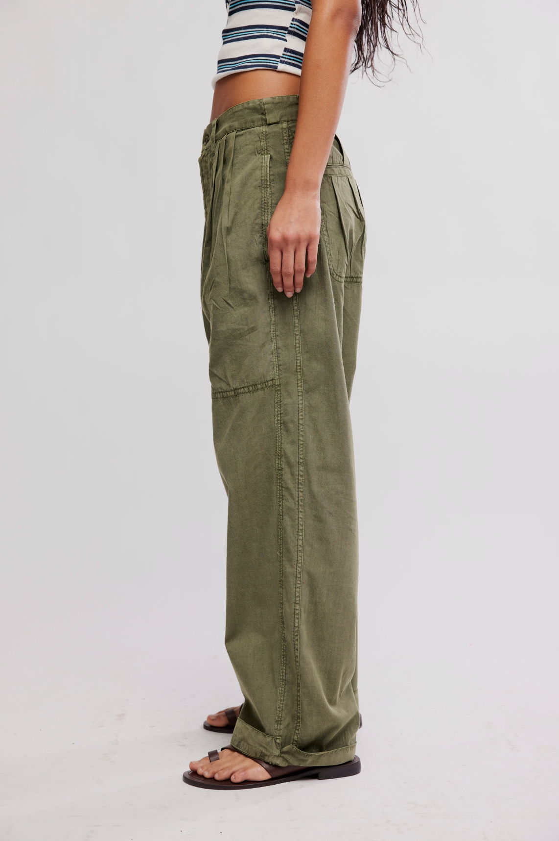 Side view of olive green loose fit Clover Dropped Trouser by Free People worn with striped crop top and sandals
