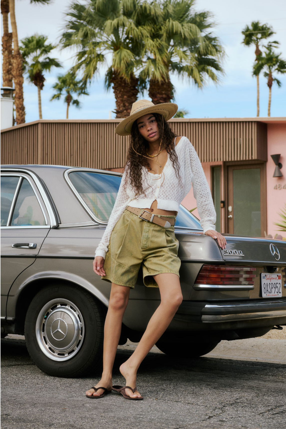 Woman wearing Wild Rebel Short in Outlaw Taupe with a white knit top and wide-brimmed hat leaning on a vintage car outdoors