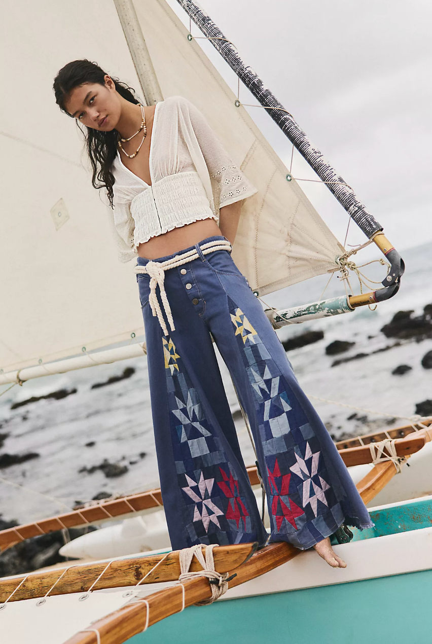 Woman wearing Wild Rebel Jean by Free People – We The Free with patchwork design standing on a boat near rocky shore.