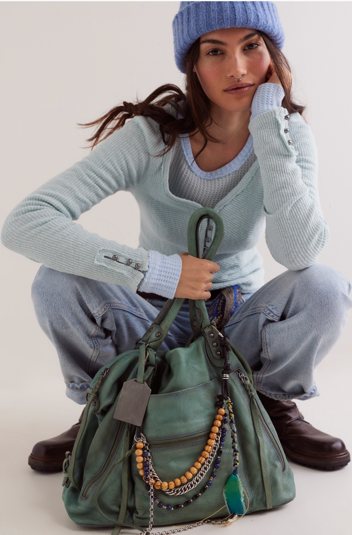 Stylish woman holding We The Free Emerson Tote Bag in Secret Sage with wooden beads and chain details on front pocket.