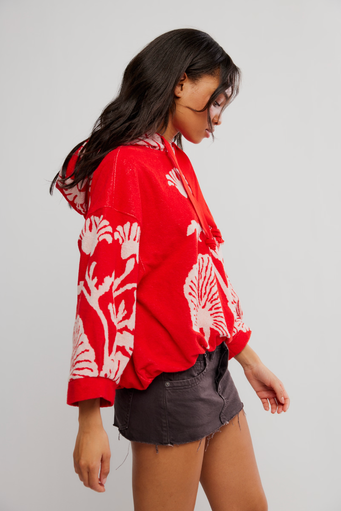 Woman wearing a red Shell Baby Hoodie with white shell patterns paired with a black denim mini skirt in studio light