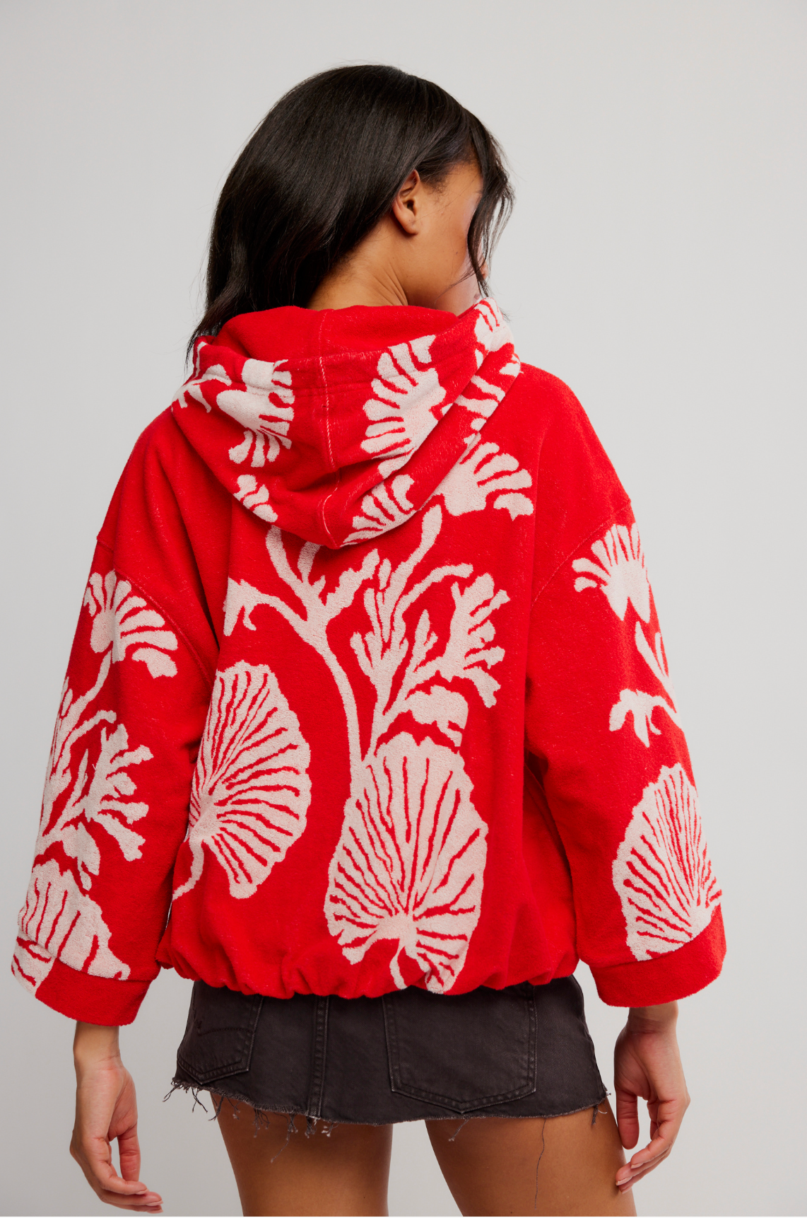 Woman wearing a vibrant red Shell Baby Hoodie with bold white shell patterns and a relaxed fit from the back view.