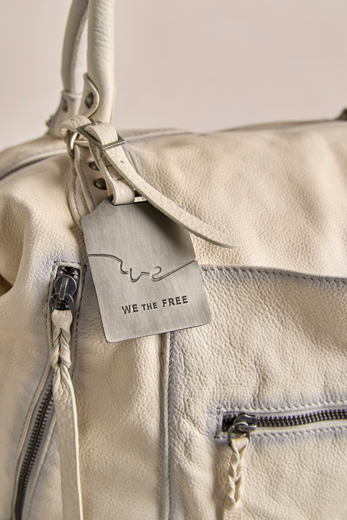 We The Free Emerson Tote Bag in Salt close-up showing soft textured leather and metal tag with brand engraving.