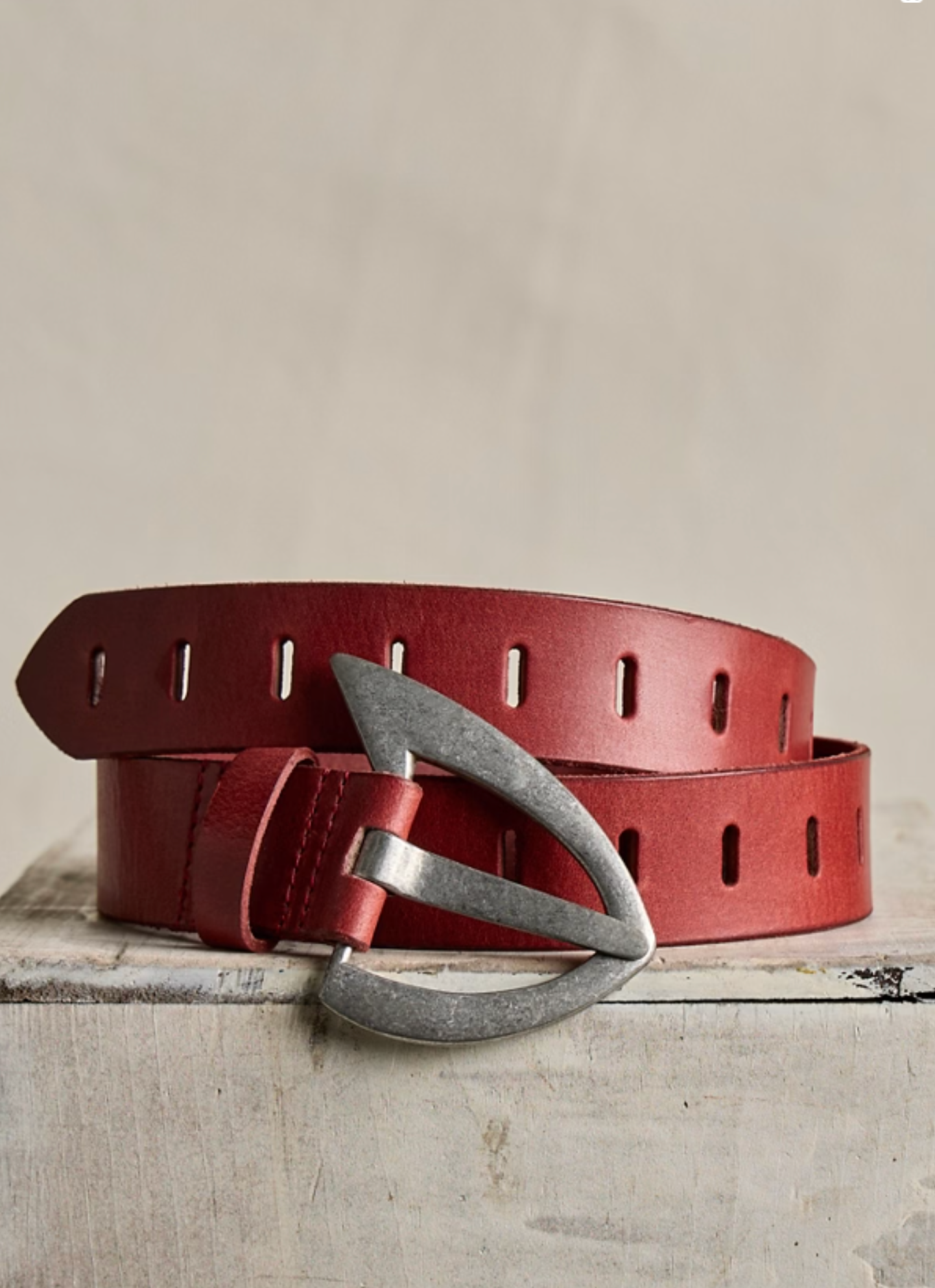 We The Free Noa Belt in Crimson with a distinctive triangular silver buckle on textured red leather background