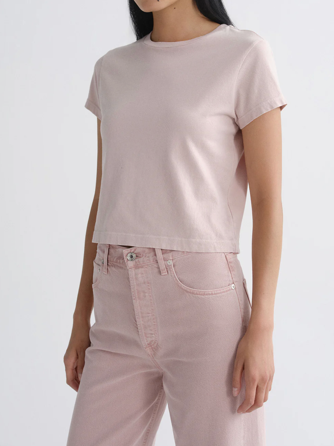 Model wearing The Adine Shrunken Te in Wallflower by AGOLDE, featuring soft fabric and a cropped fit in muted pink tones.