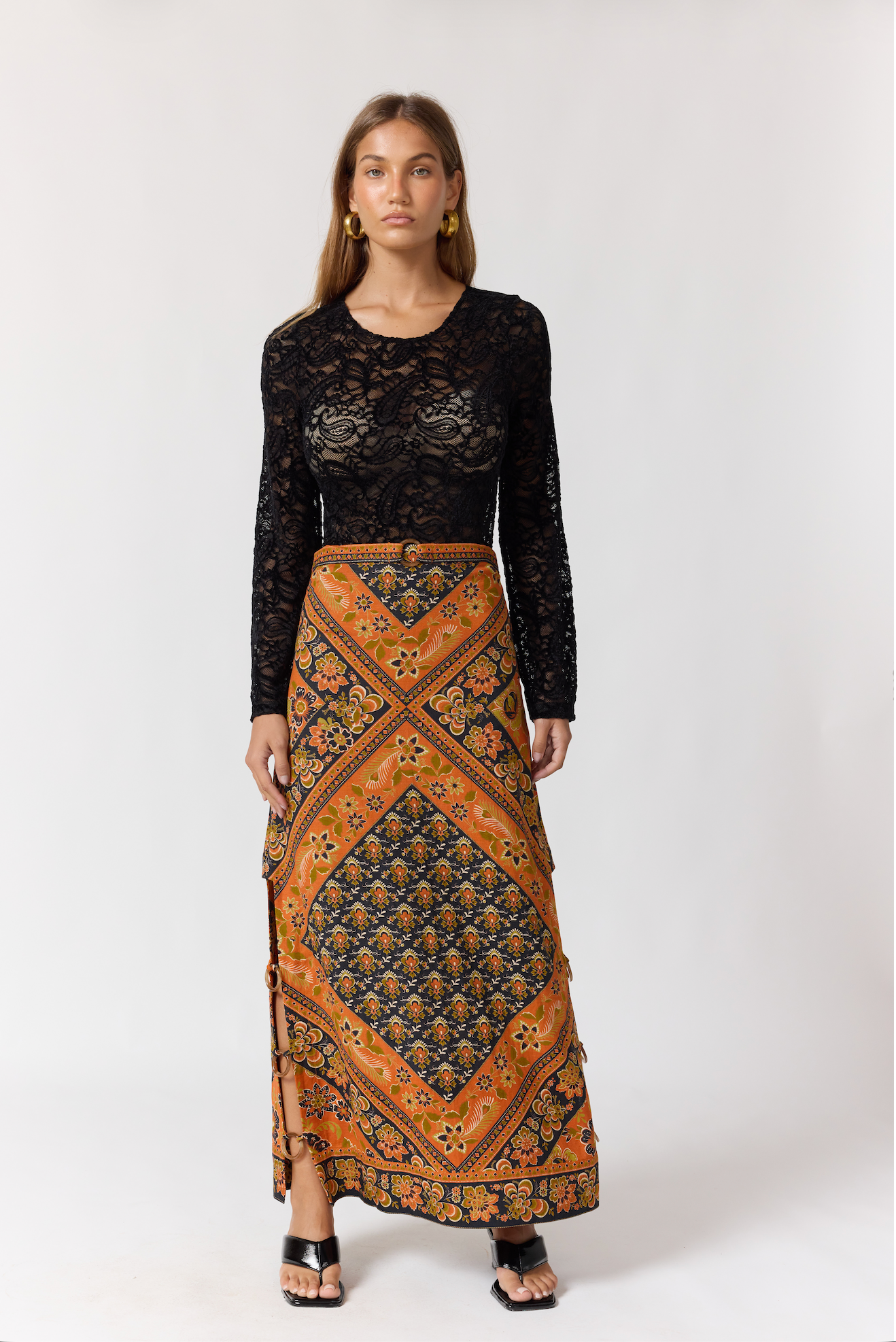 Woman wearing a colorful patterned Whitney Skirt in Saffron paired with a black lace top and gold earrings.