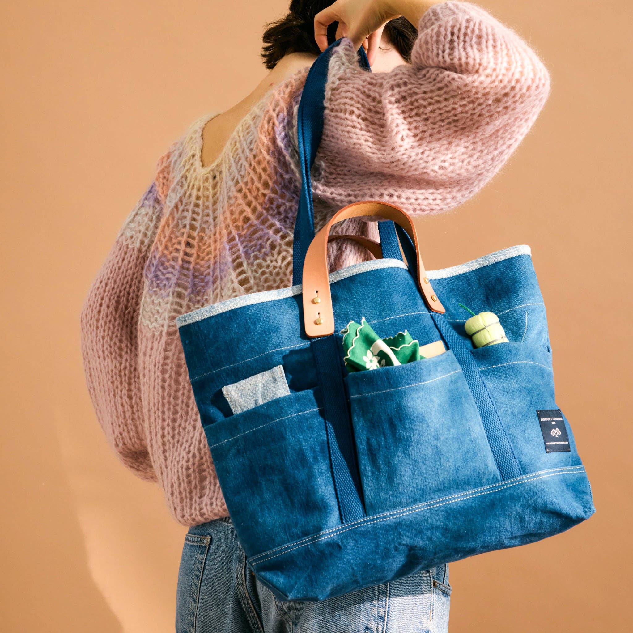 Person holding a blue tote bag with a brown handle against a beige background