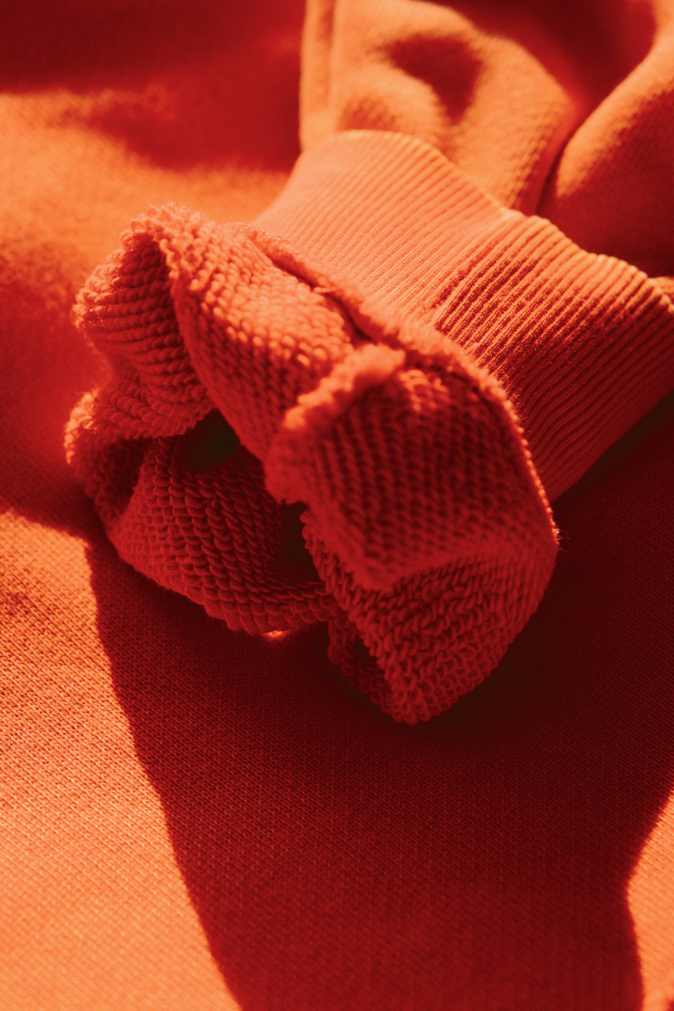 Close-up of soft textured orange fabric and ribbed cuff detail of SORRY MOM HOODIE - PRESALE in warm light.