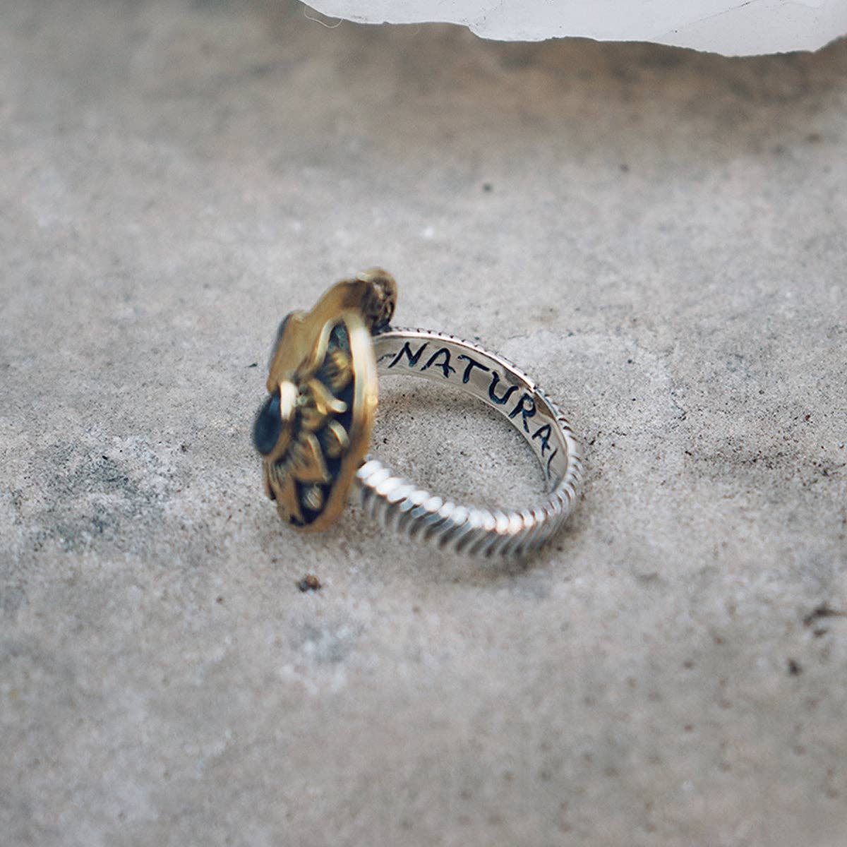 The bahgsu jewels Natural Mystic Ring - Moonstone is a sterling silver, adjustable two-toned ring with gold flower accents and NATURA engraved inside, elegantly reflecting nature’s beauty on a rough stone surface.