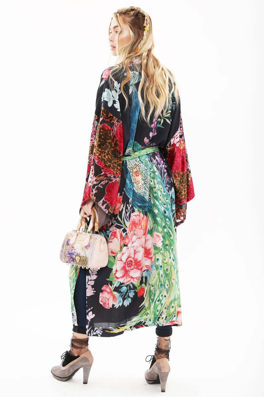A woman with long blonde hair faces away, wearing the Aratta Sweet Fantasy Kimono with burnout velvet sleeves. She holds a beige purse and wears high heels with ankle socks, set against a plain white background.