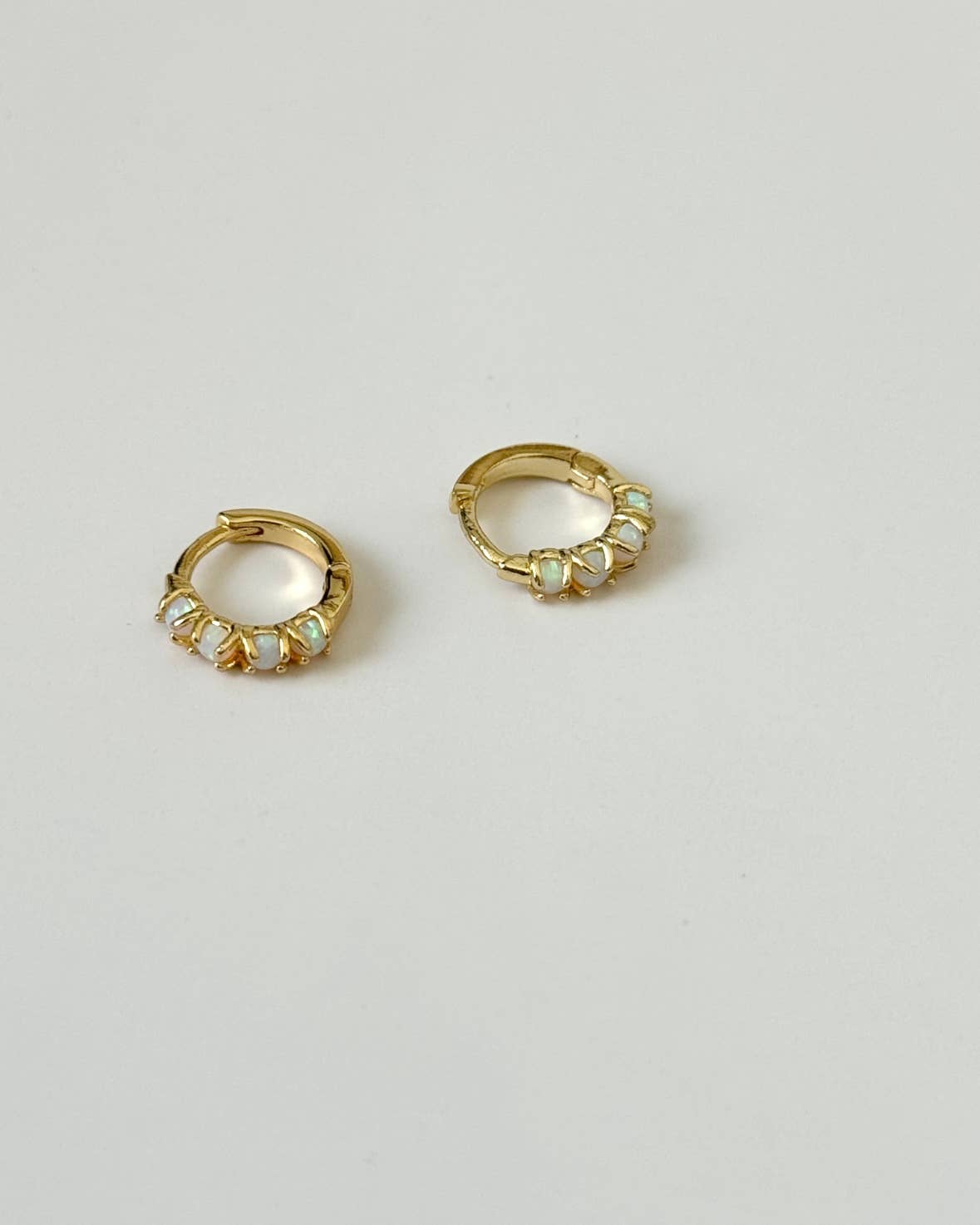 The Sonata Opal Hoops by Tramps+Thieves are gold miniature huggie earrings, each adorned with five iridescent opal stones, shown on a simple, light background.