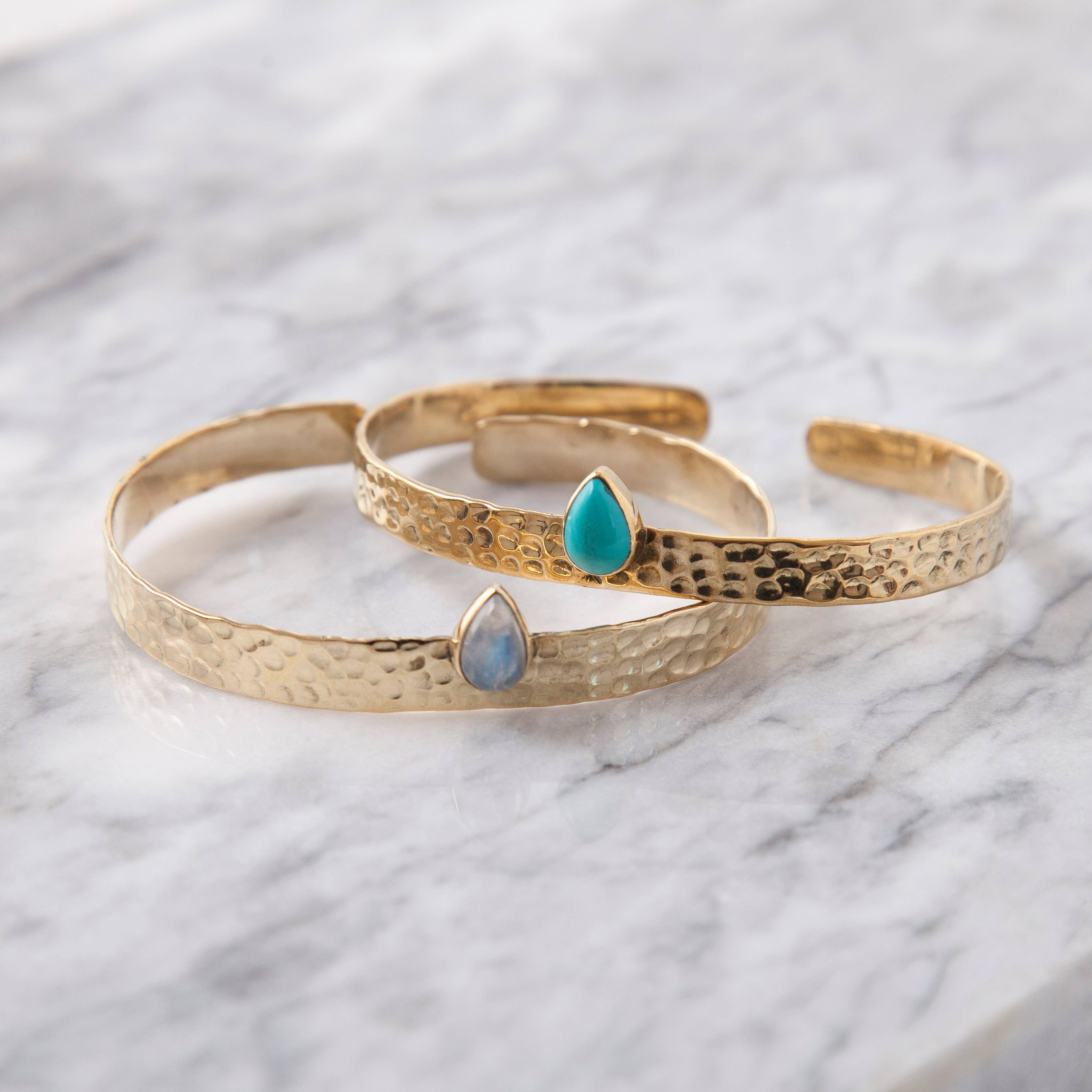 Brass Hammered Cuff with Tear Drop Stone featuring textured metal bands with blue and turquoise teardrop accents on marble surface
