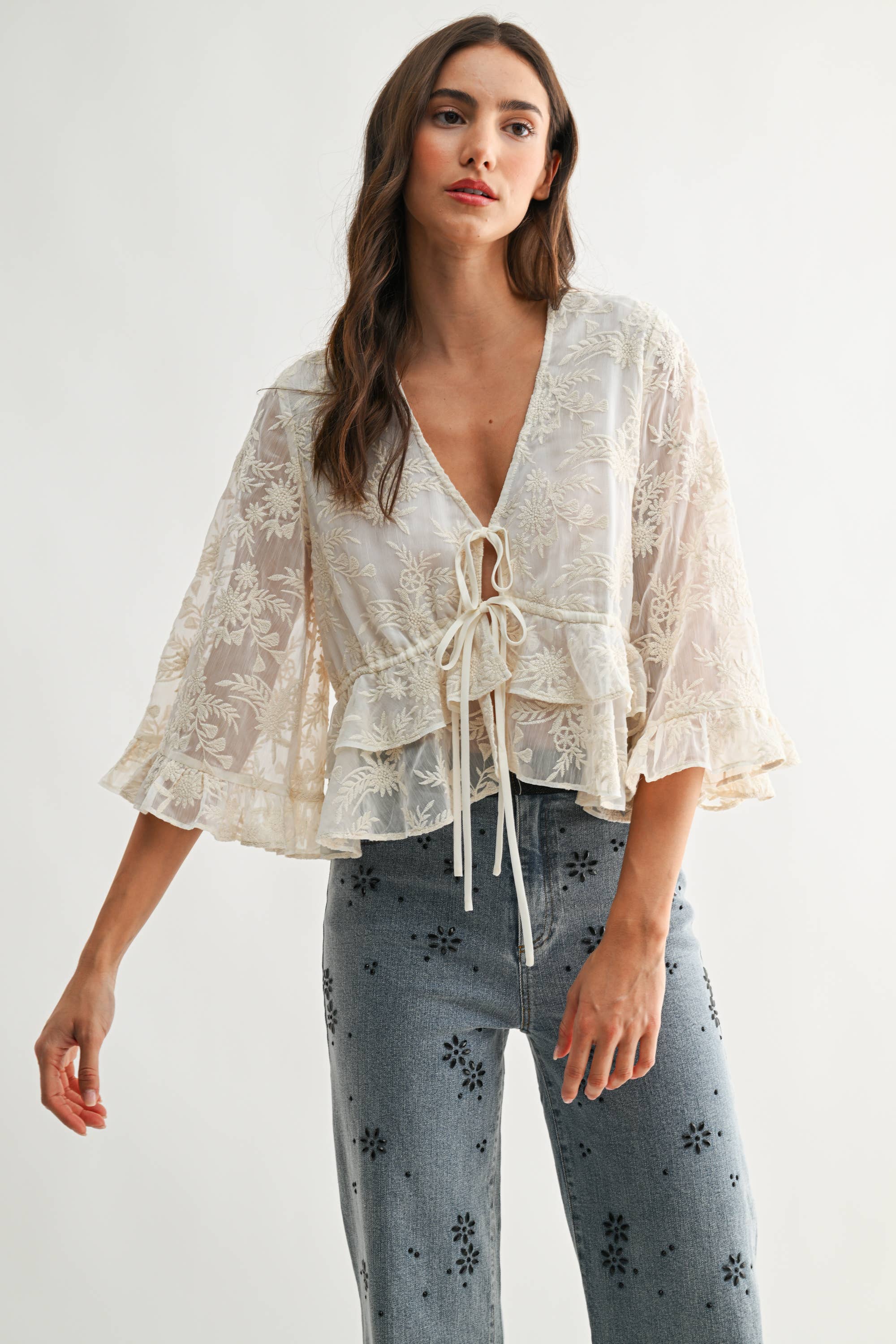 Woman wearing Boho Embroidered Sheer Blouse with floral embroidery and ruffled sleeves paired with patterned jeans