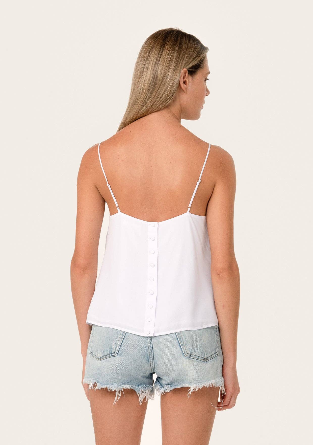 Woman wearing Button Back Embroidered Lace Cami with thin straps paired with light denim shorts, back view