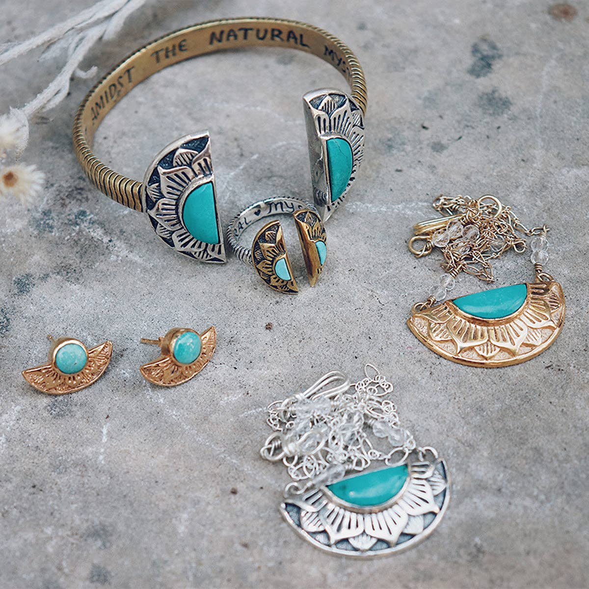 A selection of bahgsu jewels’ silver and gold pieces—featuring the Natural Mystic Ring - Turquoise, bracelet, earrings, and necklaces with turquoise accents—displayed on a textured stone surface.