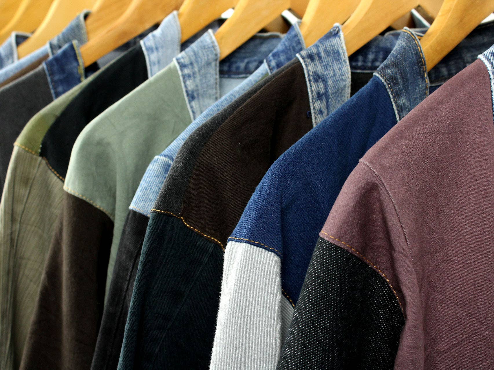 Row of colorful upcycled patchwork denim jackets hanging on wooden hangers in a boutique setting