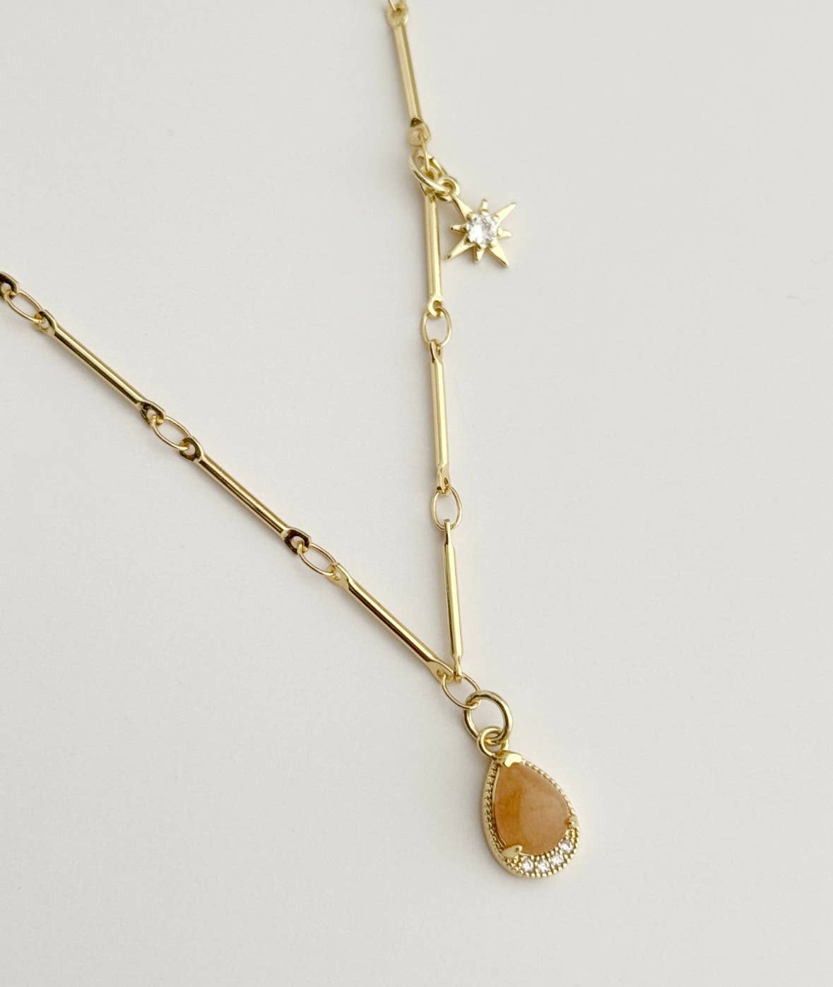 The Stone From The Sun Necklace by Tramps+Thieves features a teardrop pendant and star charm with sparkling CZ, on an 18K gold-filled chain, shown against a light neutral background.