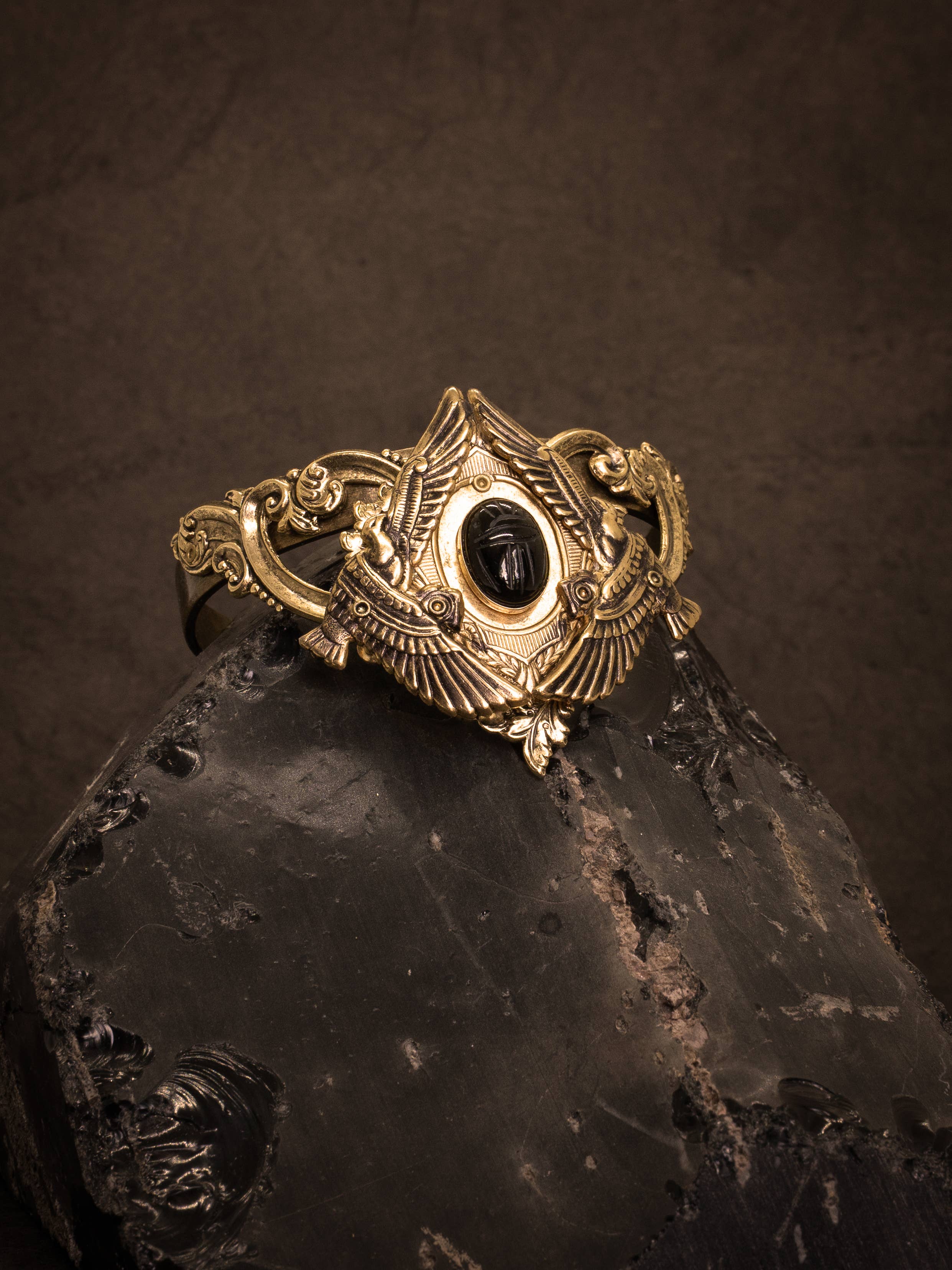 Nekhbet Shield Cuff featuring intricate gold details and a central black stone on a dark textured surface
