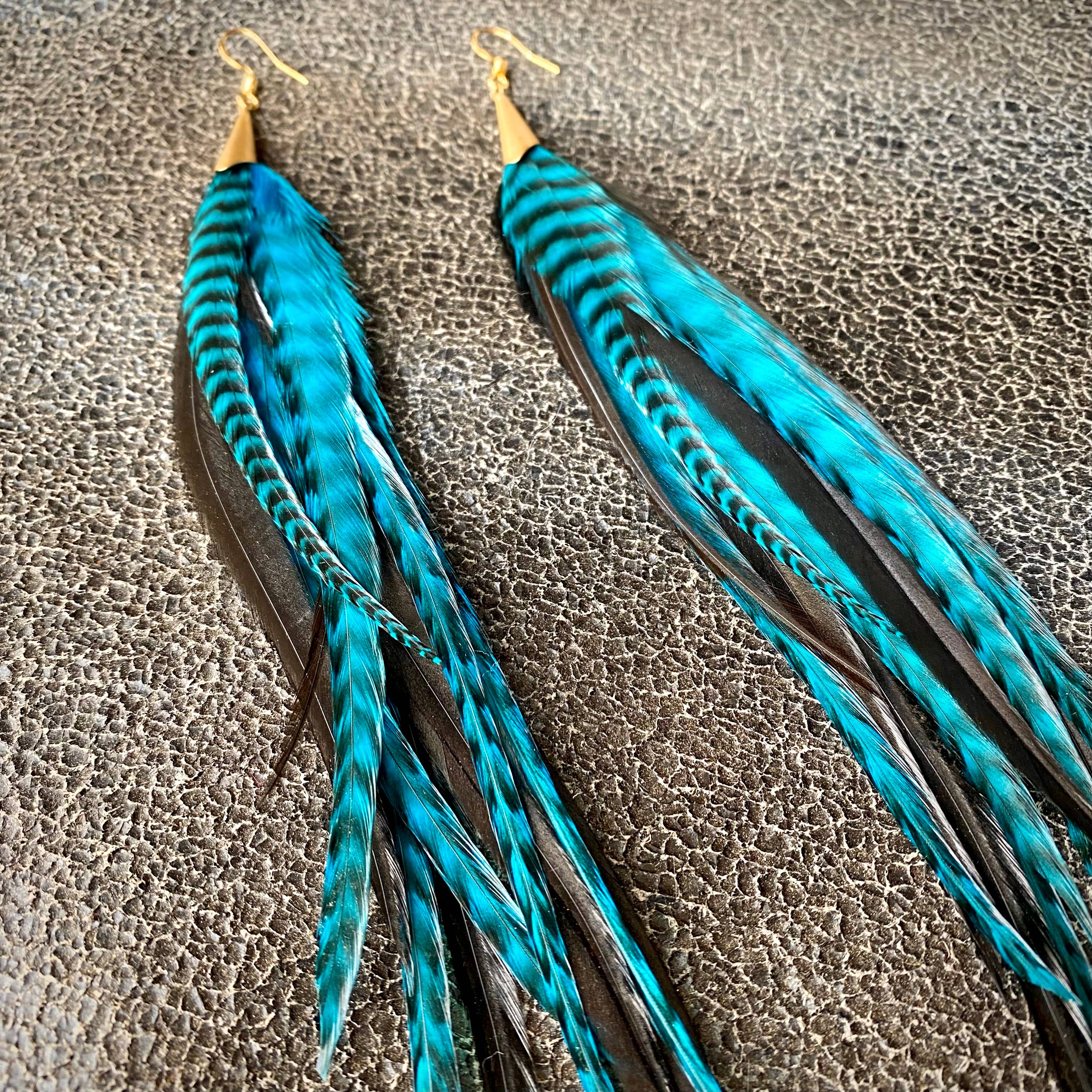 ASTALI Long Feather & Cone Earrings - Turquoise Grizzly & Black/Gold feature sustainably sourced turquoise and black feathers with gold hooks, shown on a textured dark gray background.