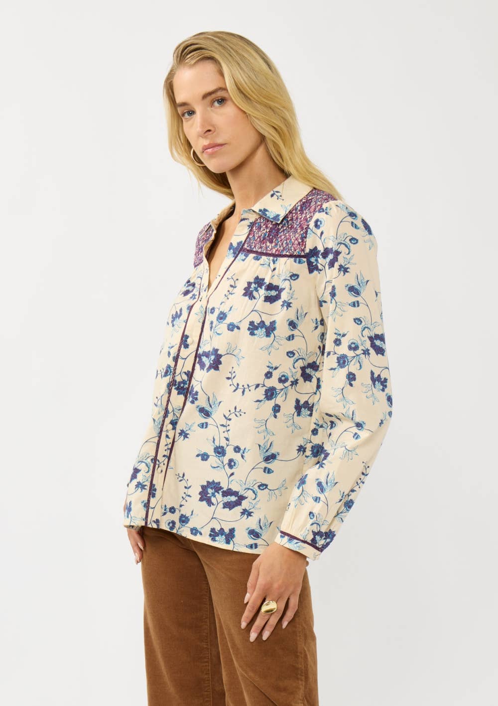 Woman wearing a Long Sleeve Floral Blouse with Smocked Yoke in cream with blue and purple floral patterns.