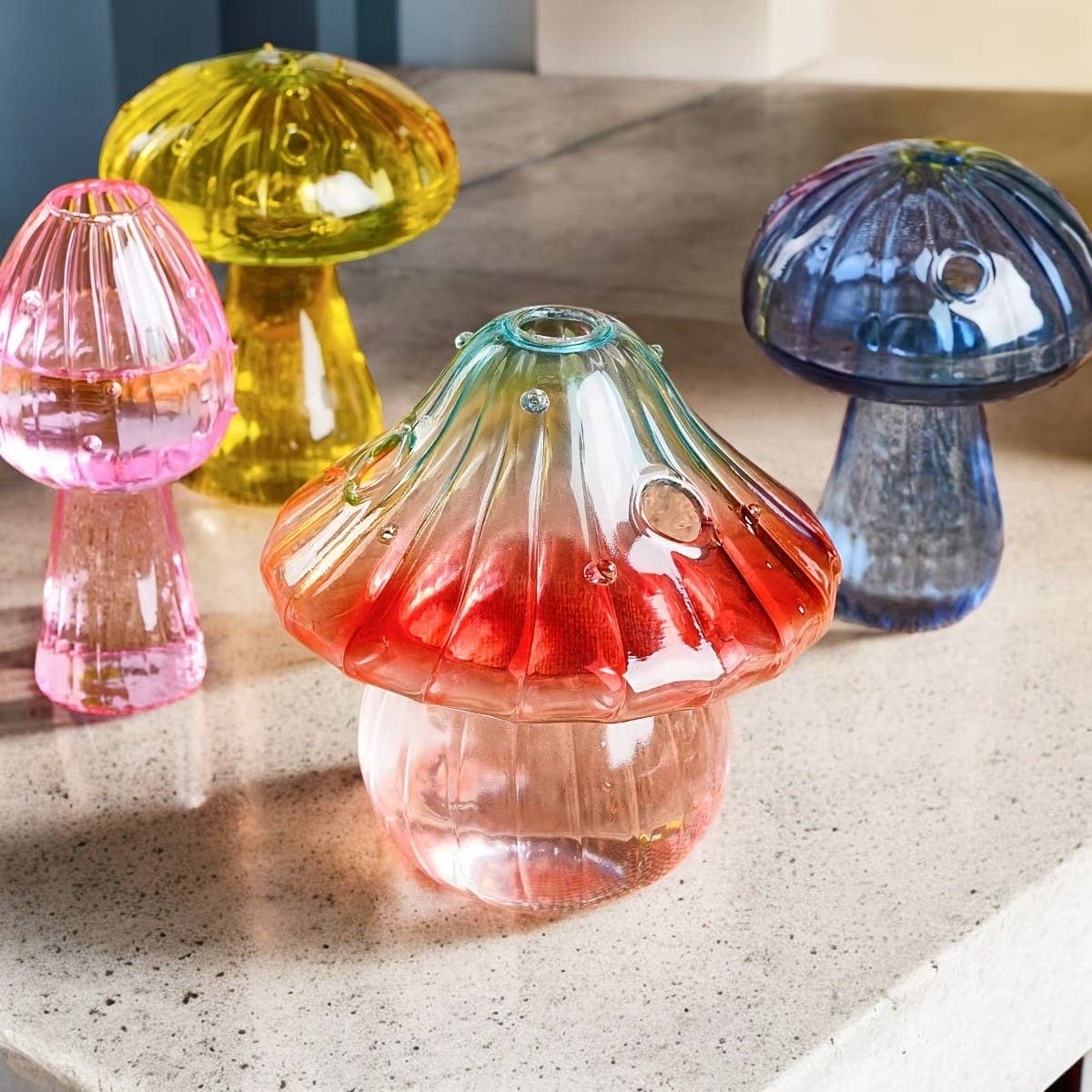 Multi Color Mini Glass Mushroom Bud Vase in vibrant translucent pink, yellow, blue, and red hues displayed on a smooth surface.