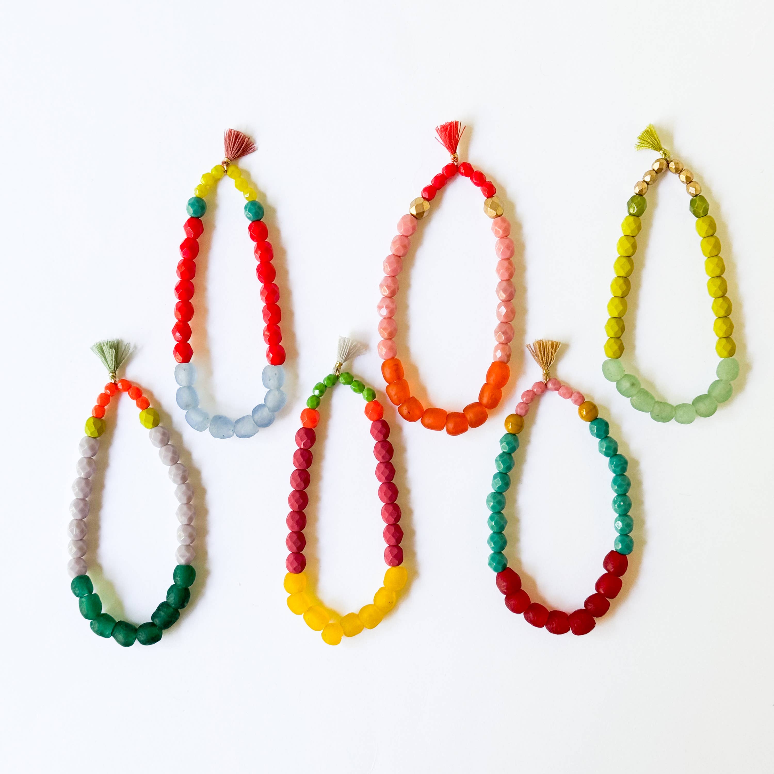 Six colorful Multicolor Recycled African Glass And Mixed Bead Bracelet strands arranged with tassel details on a white background.