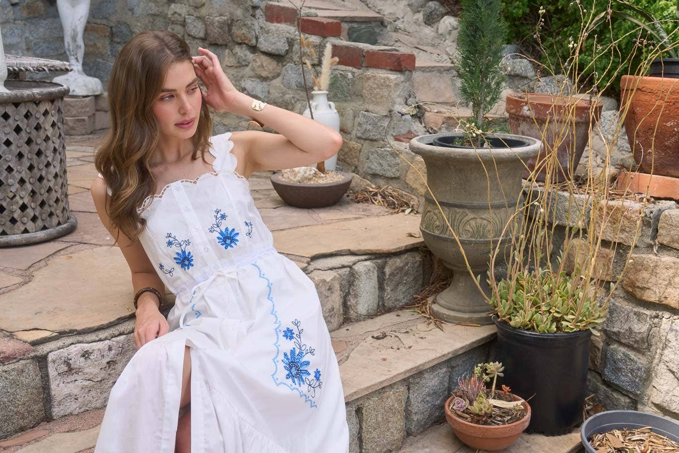 Woman wearing The Molly Embroidered Detail Midi Dress with blue floral embroidery sitting outdoors on stone steps