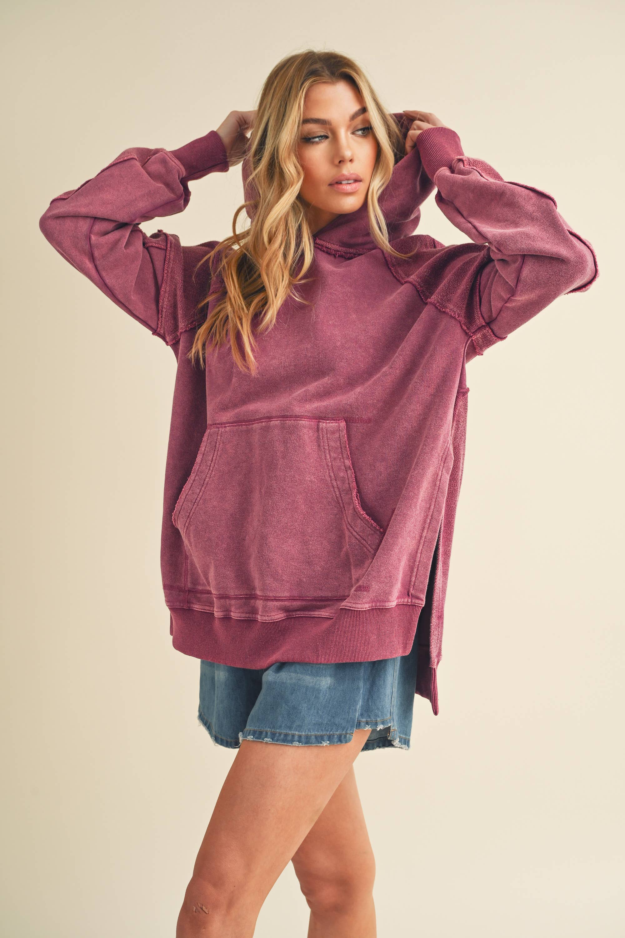 Woman wearing a faded purple Deb Washed Hoodie with kangaroo pocket and relaxed fit paired with denim shorts