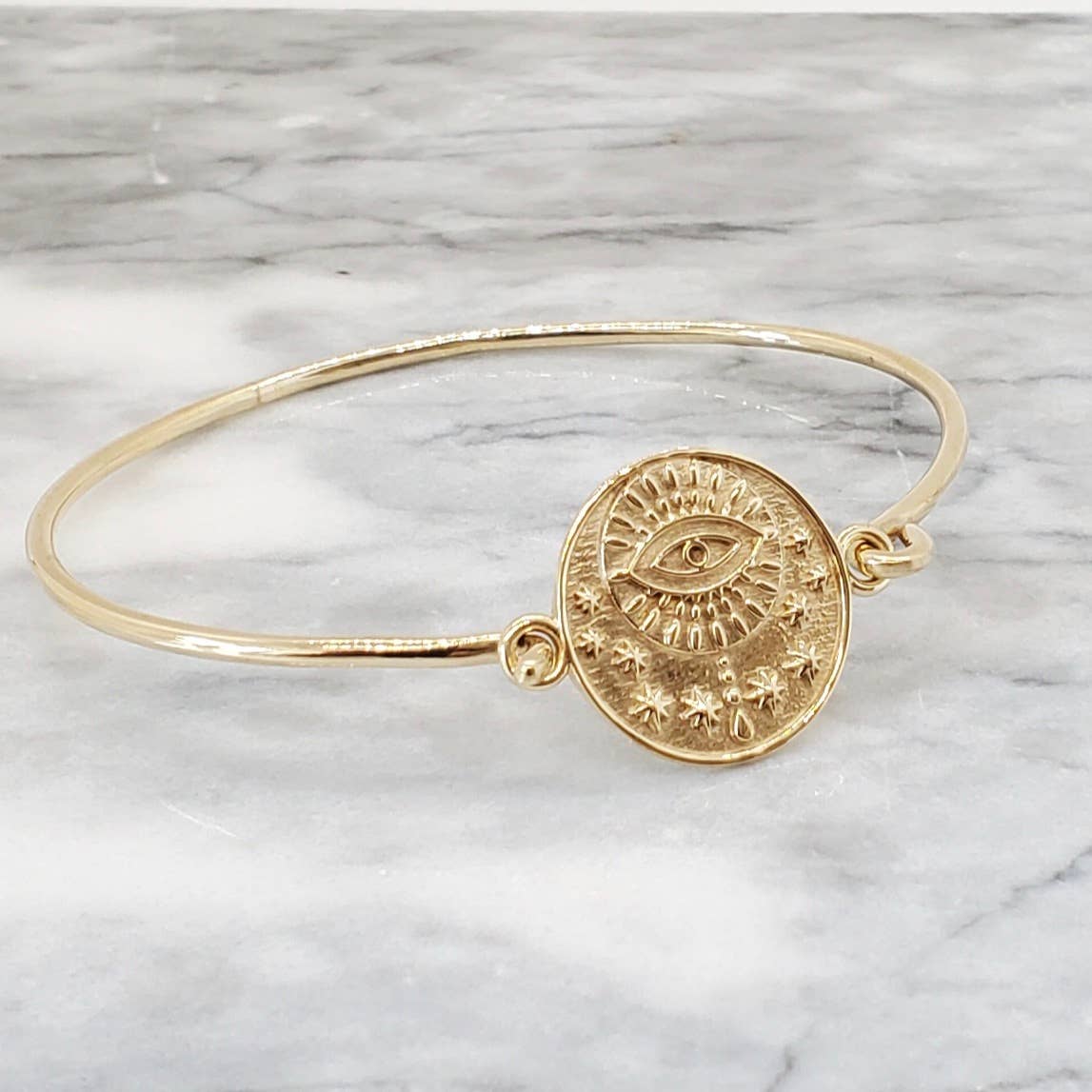 The Evil Eye Medallion Bracelet in Brass by Baizaar, a unique handmade piece featuring an engraved all-seeing eye with rays and stars, is the perfect boho jewelry gift—especially for Hanukkah!.