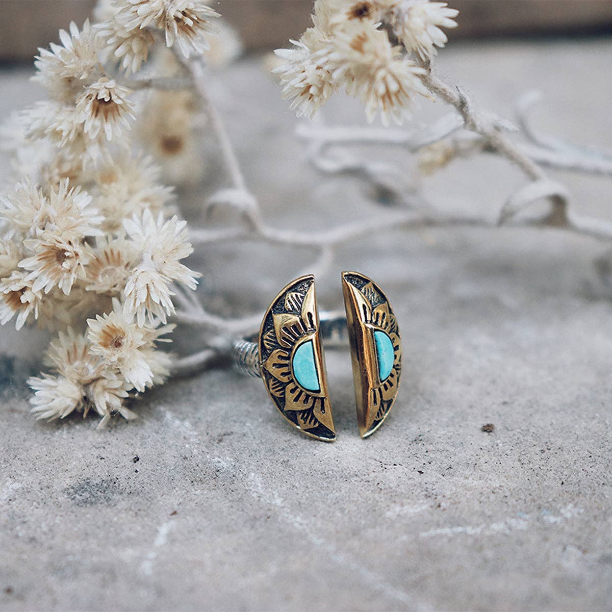 Half-moon gold and black sunburst earrings with turquoise stones, shown on stone beside dried white flowers—perfectly matched with the bahgsu jewels Natural Mystic Ring - Turquoise for a boho-chic look.