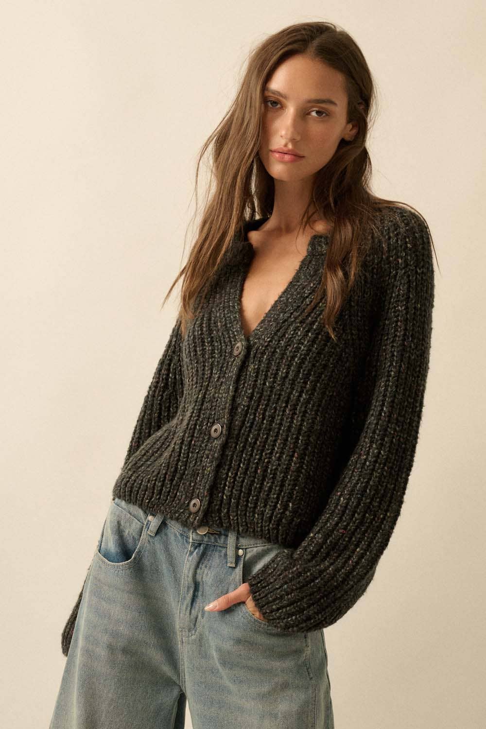 A woman with long brown hair wears the Promesa USA Confetti Button-Front Cardigan Sweater and light blue jeans, standing against a neutral background with one hand in her pocket.