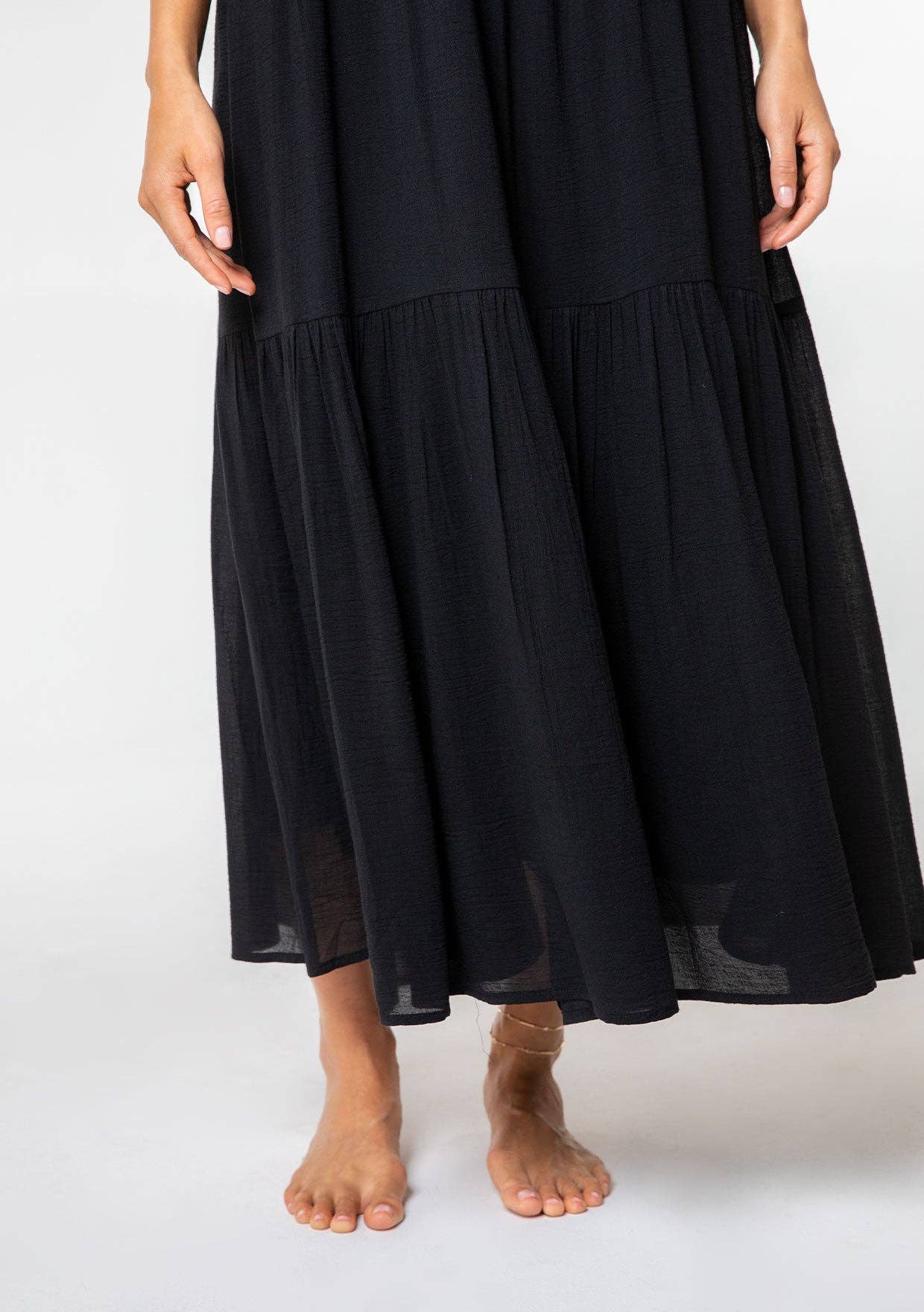 Close-up of black Bohemian Crochet Tiered Maxi Dress flowing around bare feet on white background