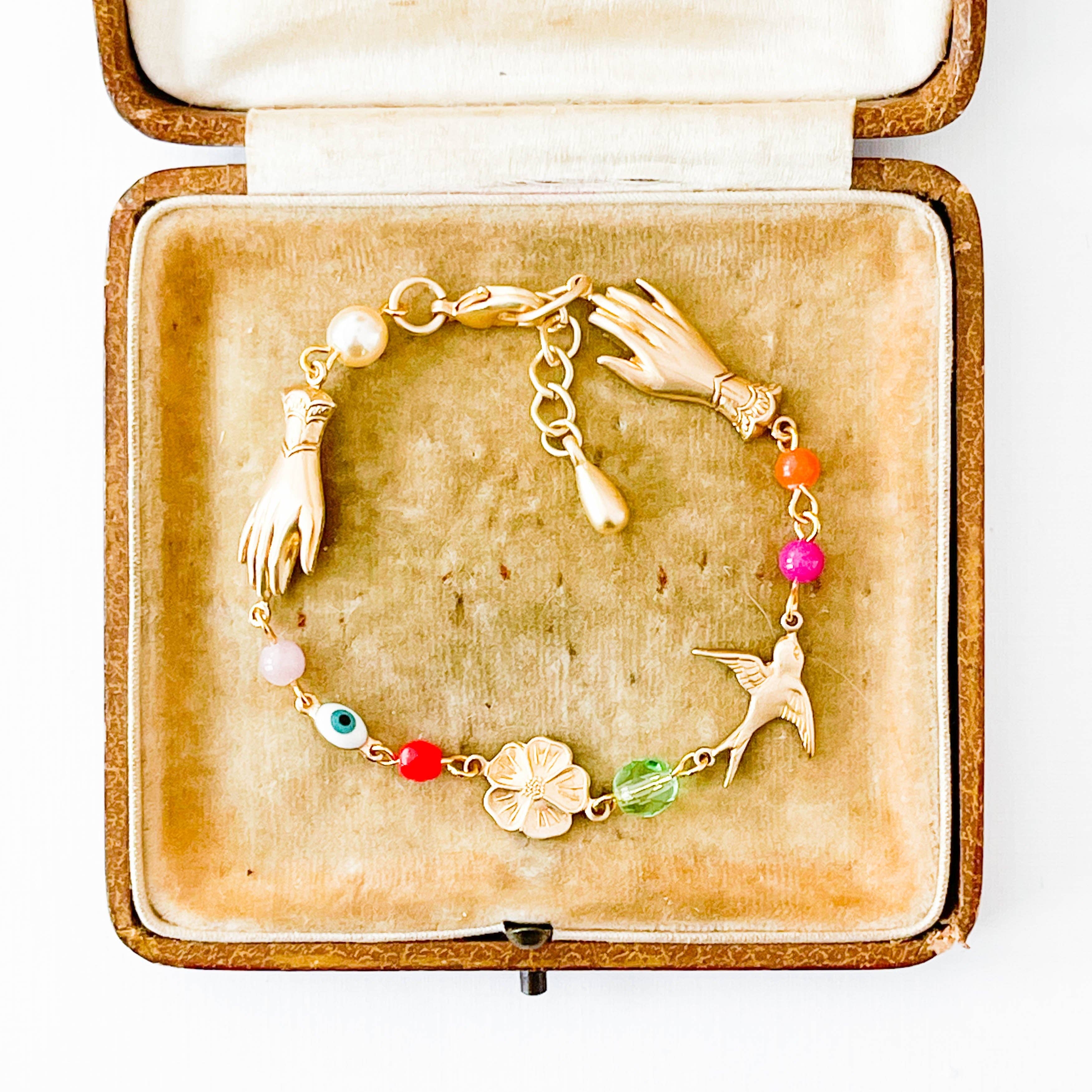 Adjustable Evil Eye Charm Bracelet With Pearl And Beads displayed in a vintage velvet jewelry box with colorful charms and gold hands