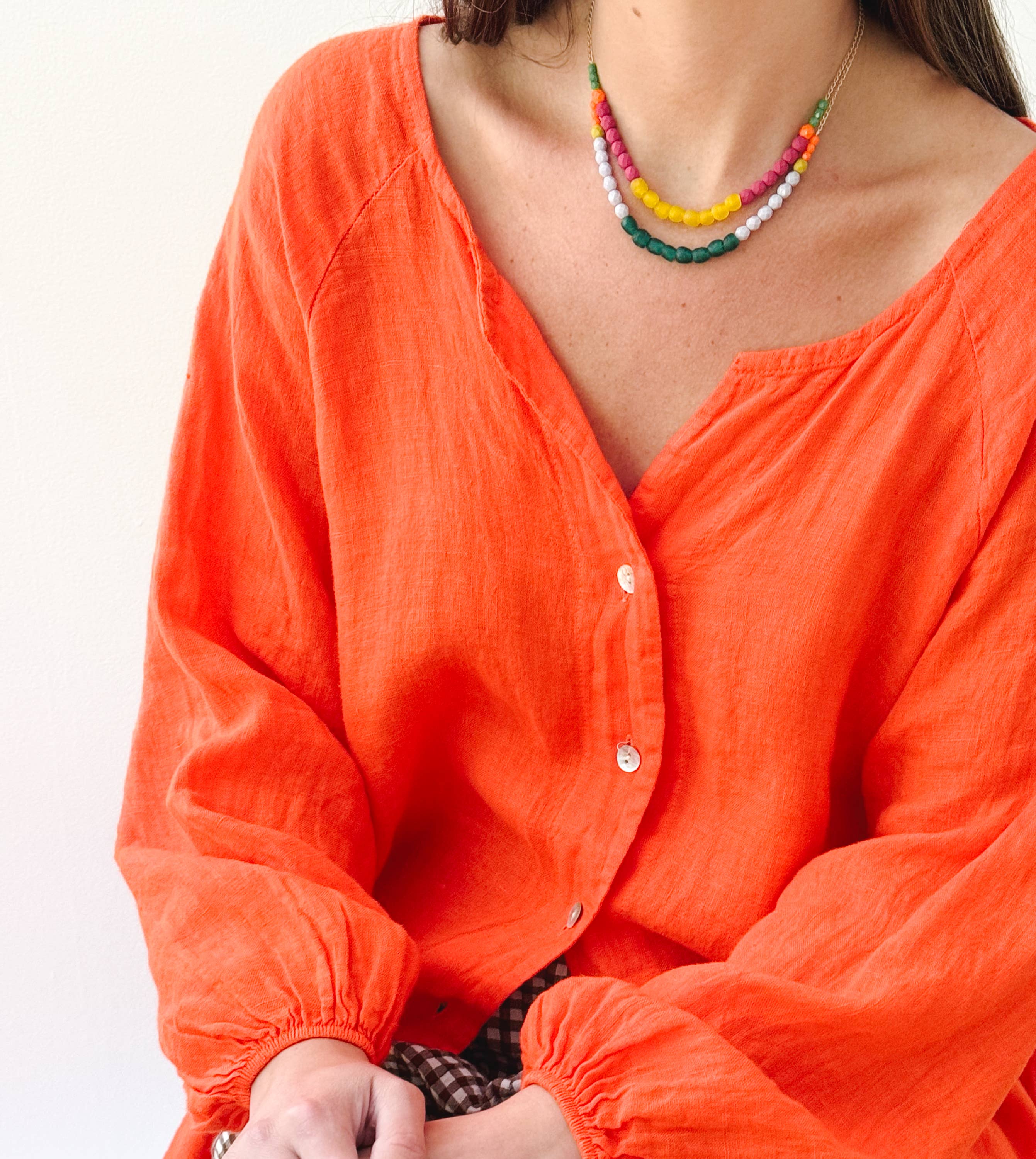 Woman wearing colorful layered beads with Multicolor Recycled African Glass And Mixed Bead Necklace and bright orange blouse