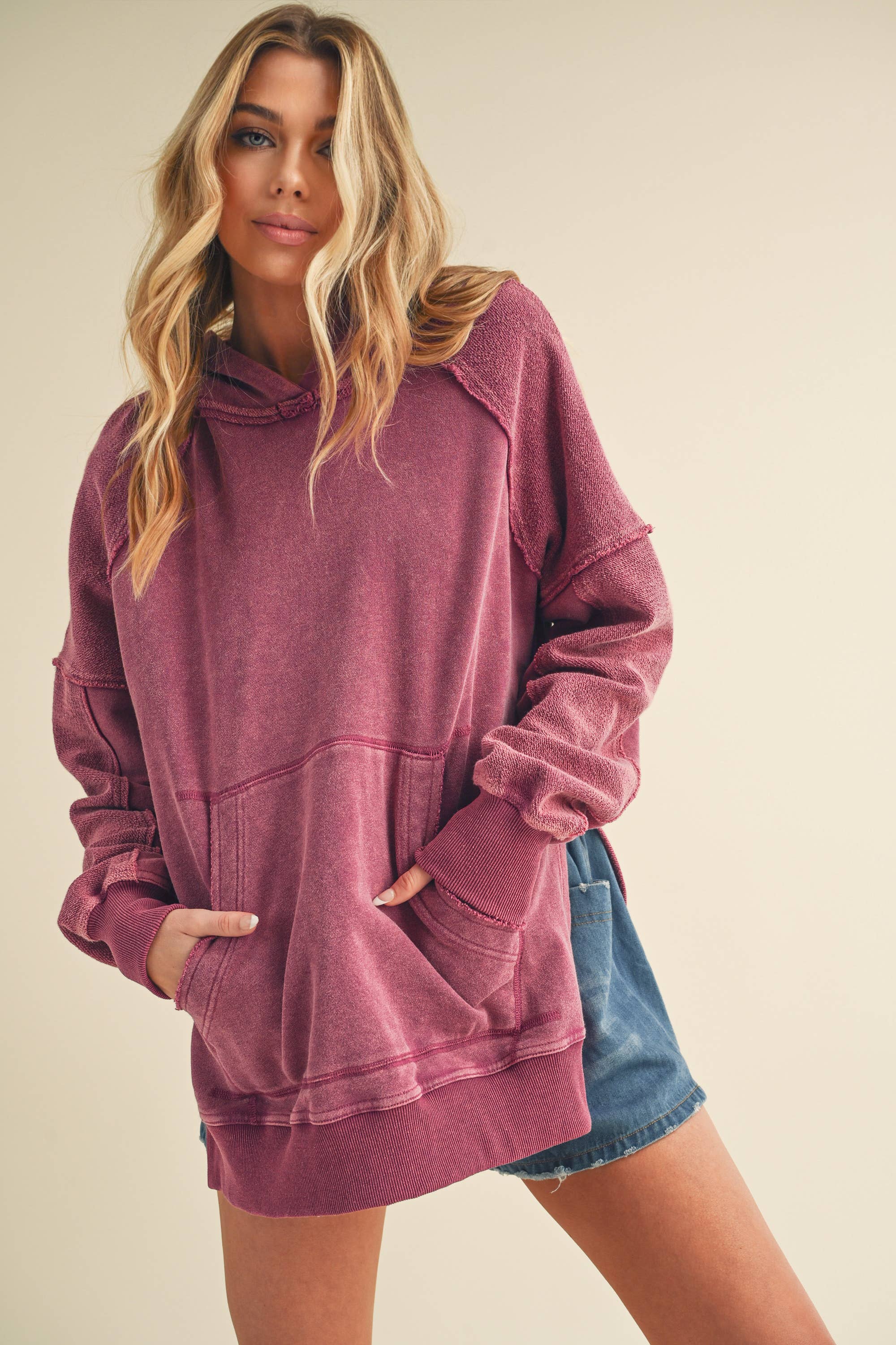 Woman wearing a cozy faded purple Deb Washed Hoodie with pockets and relaxed fit paired with denim shorts