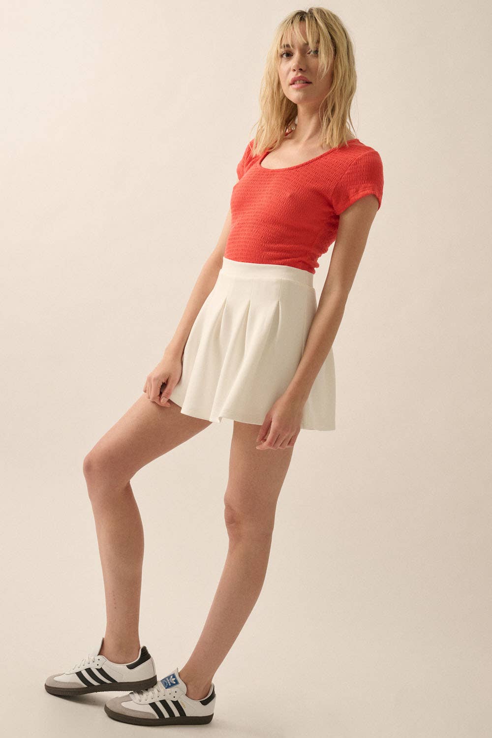 Woman posing wearing a vibrant red Smocked Jersey Scoop Neck Bodysuit paired with a white skirt and sneakers