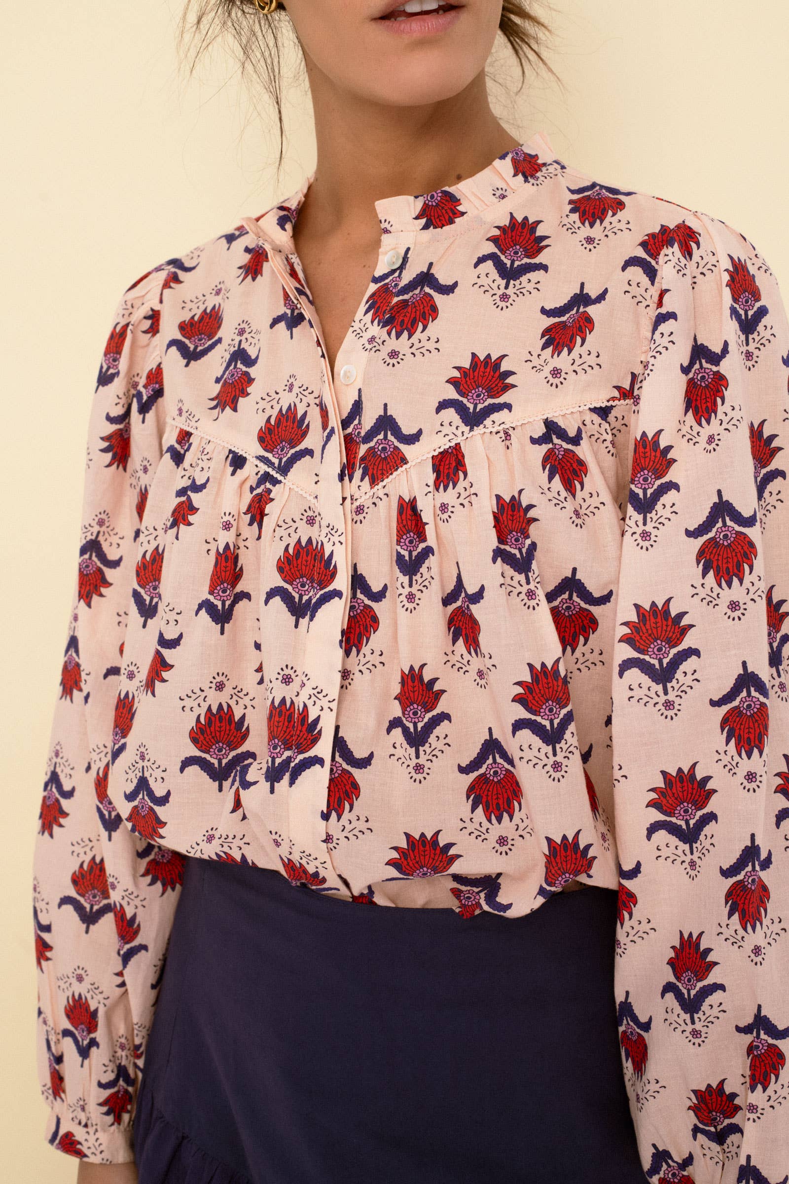 A woman wears the Sonmer Shop USA Vanessa blouse peach—long-sleeved, light pink cotton voile with a floral print—paired with a high-waisted dark navy skirt. Her face is partially out of the frame.