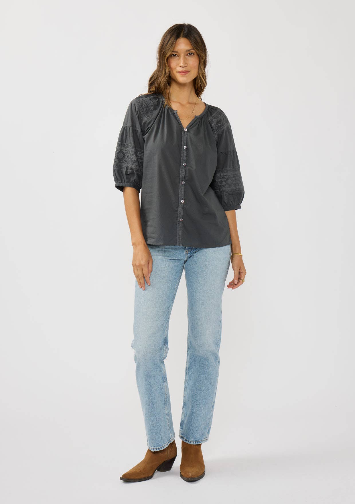 Woman wearing a Short Raglan Puff Sleeve Button Down Top in dark fabric with light blue jeans and brown boots.