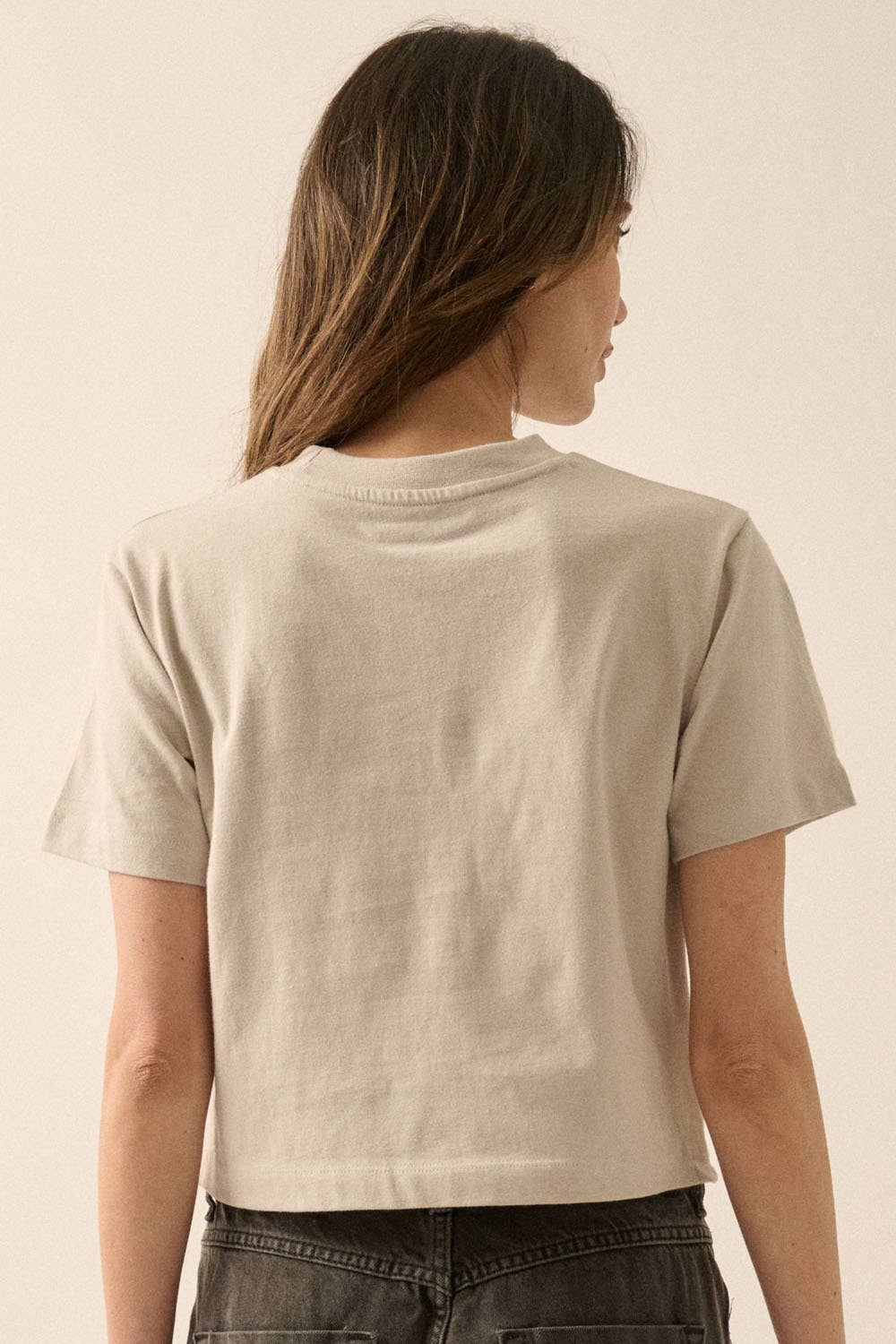 Back view of a woman wearing a soft beige Cherries Cropped Garment-Dyed Graphic Tee with short sleeves.