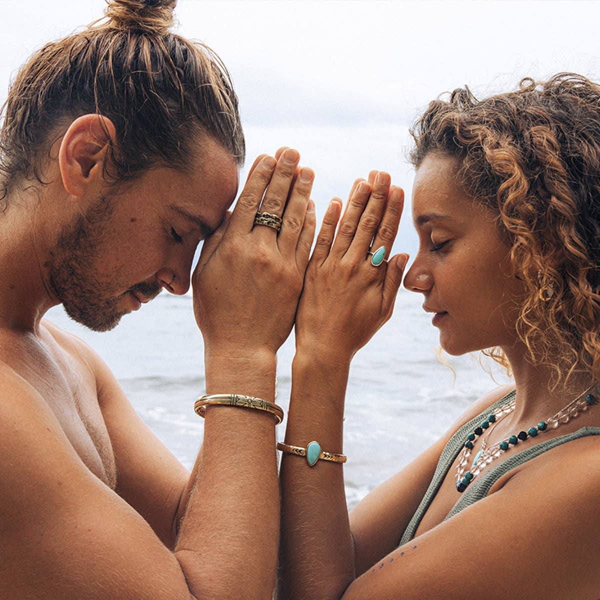 Two people facing each other with hands pressed together, one wearing a Medicine Wheel Cuff || Men bracelet outdoors by the sea.