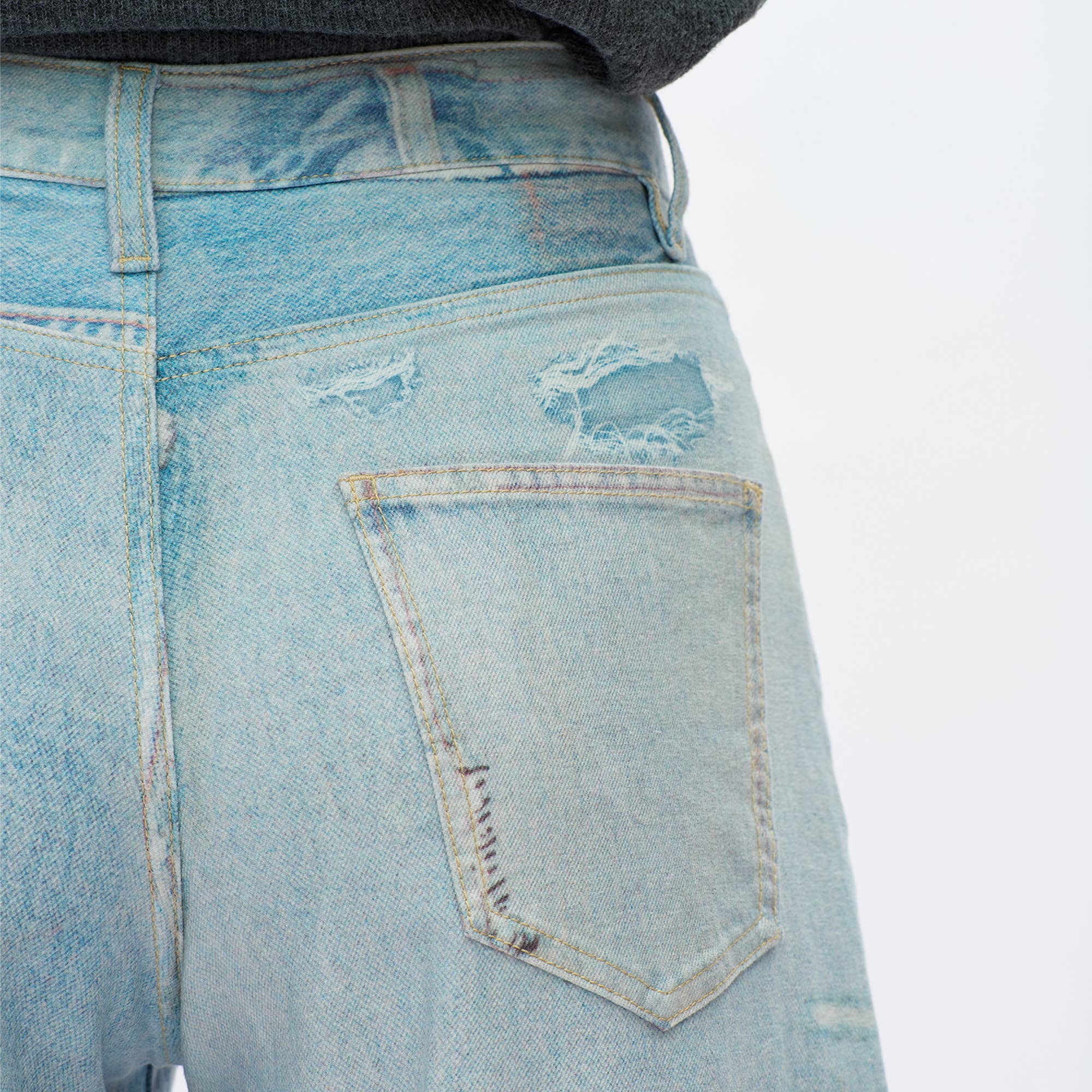 Close-up of the back of a person wearing BAYEAS Light Blue Patch Pattern High-Rise Barrel Jeans, featuring visible stitching, a faded worn texture, comfort stretch denim, and a rip above the right back pocket.