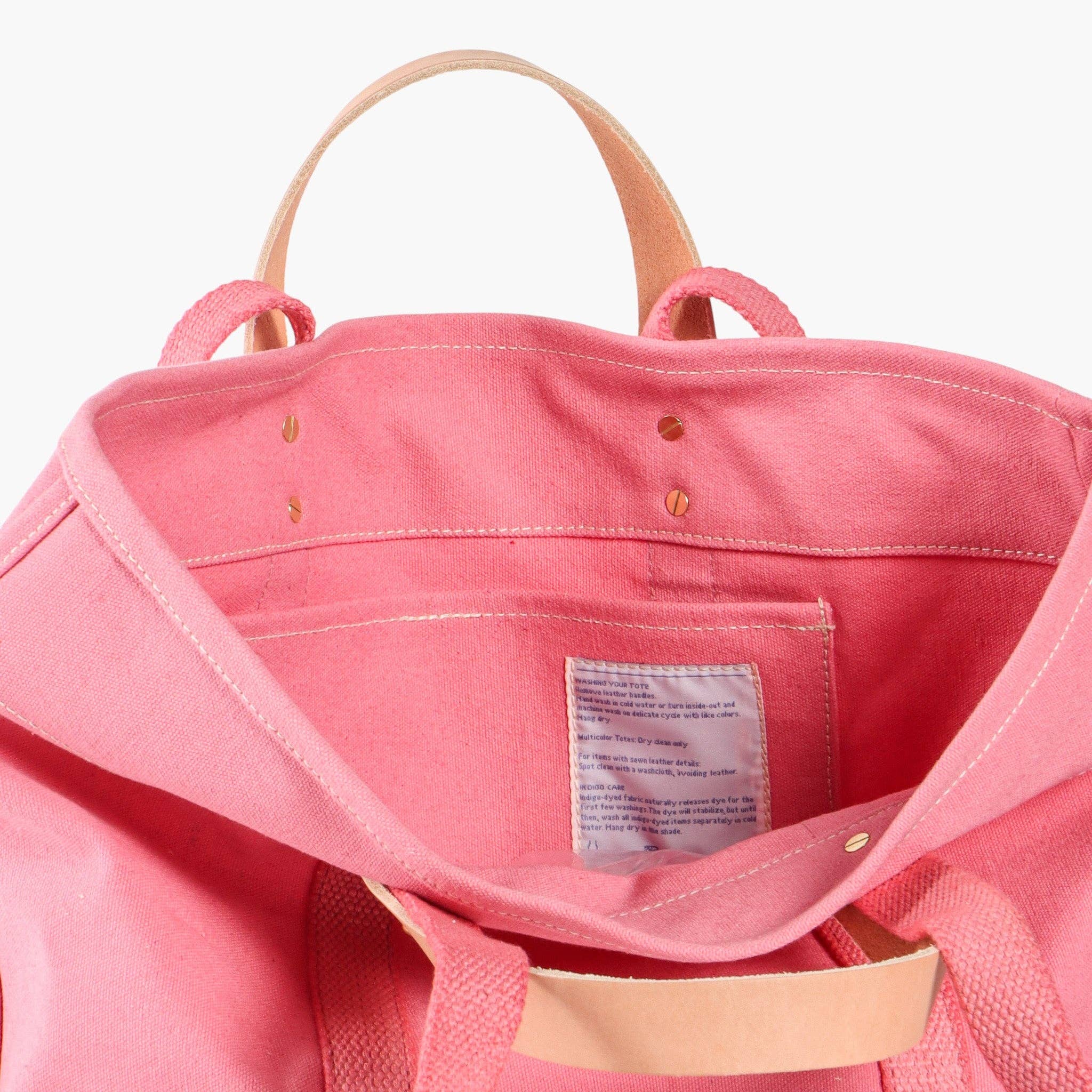 Interior view of a pink canvas bag with leather handles showing stitching and inside pocket of Small East West Tote | Flamingo