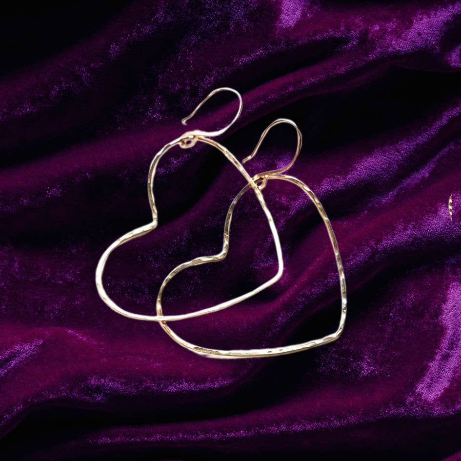 The Big Gold Heart Hoop Earrings by Dreamers of Dreams rest on deep purple velvet, creating a stunning statement look.