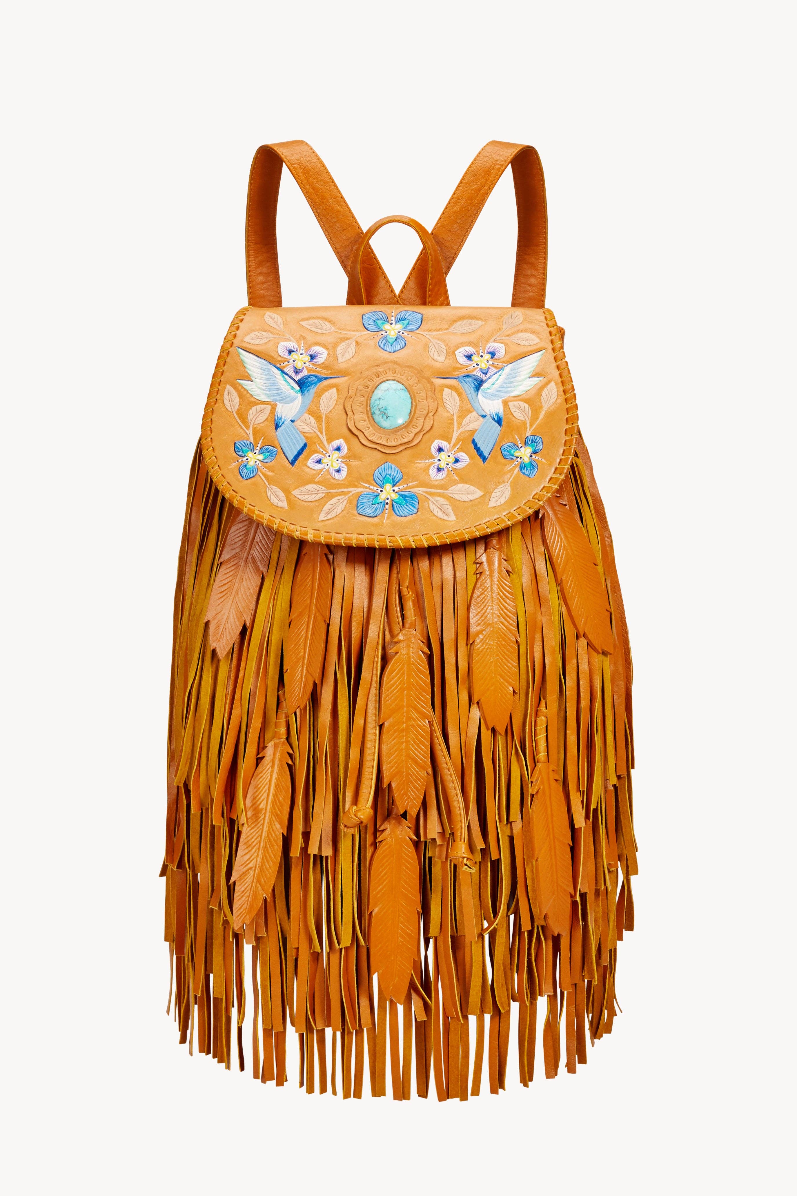 The Jodi Lee Monterey Backpack Antique Tan is a handmade leather bag with fringe, feather details, embroidered blue and white birds, floral motifs, and a turquoise stone accent on the flap, crafted from antique tan cow leather.