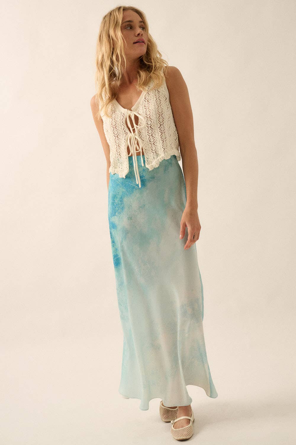Woman wearing a Tie Dye-Print Satin Bias-Cut Maxi Skirt in blue hues paired with a cream sleeveless lace top